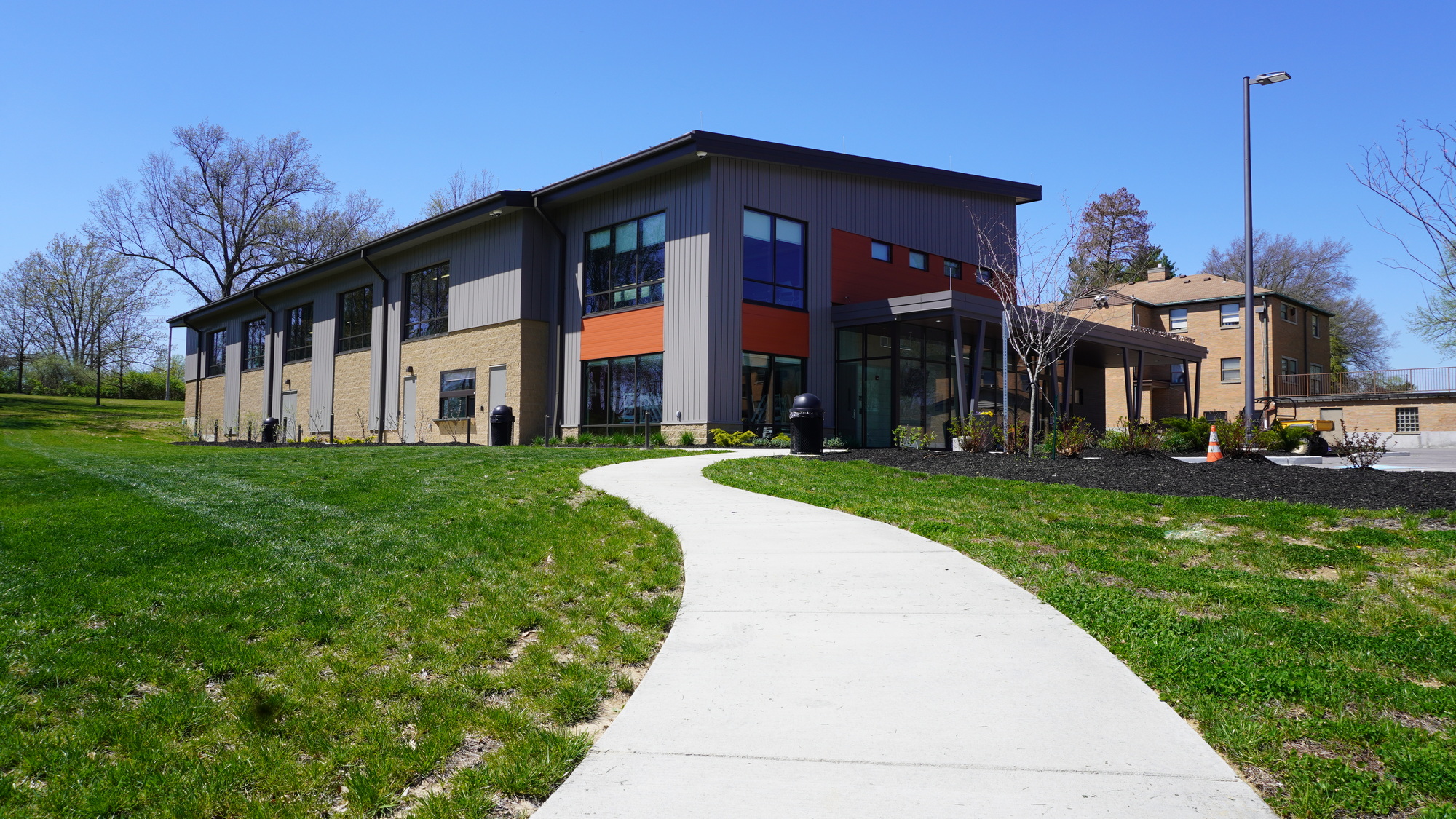 Modern building with a curved path, surrounded by grass and trees under clear sky.