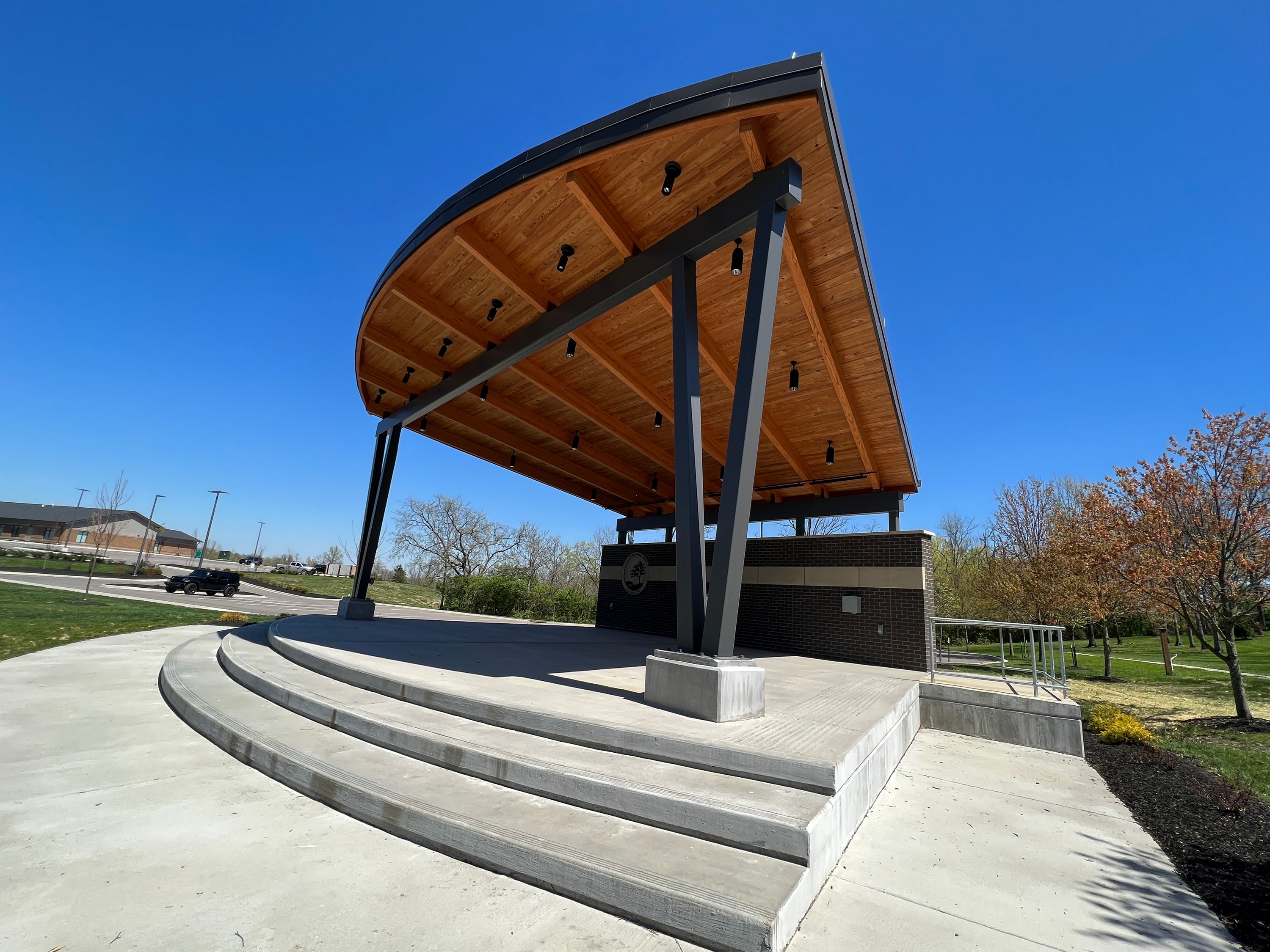 Modern outdoor stage with wooden roof and steps, set against a clear blue sky.