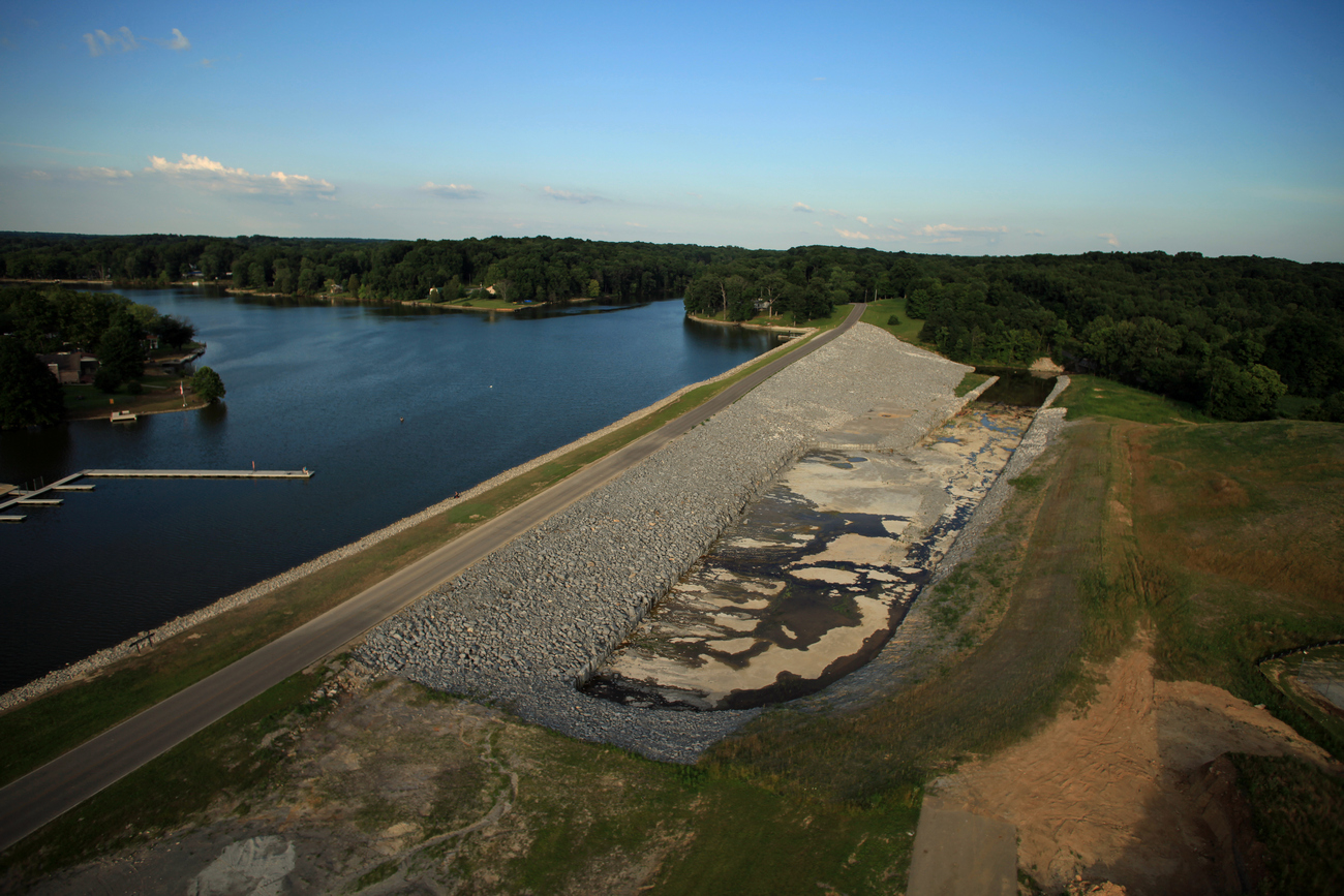 Lake and dam with surrounding forest under a clear blue sky.