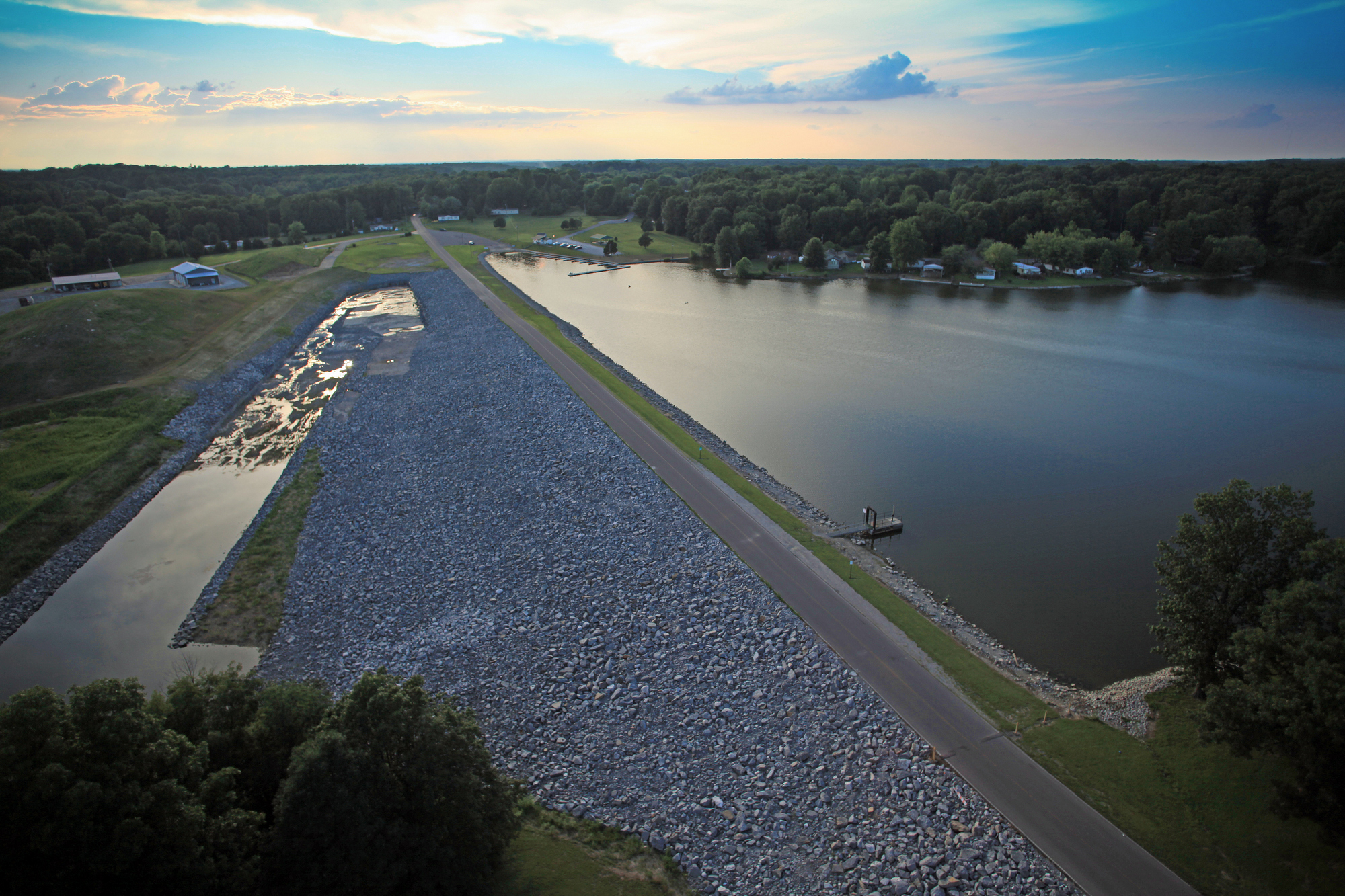 Aerial view of a dam and lake at sunset, with trees lining the water.
