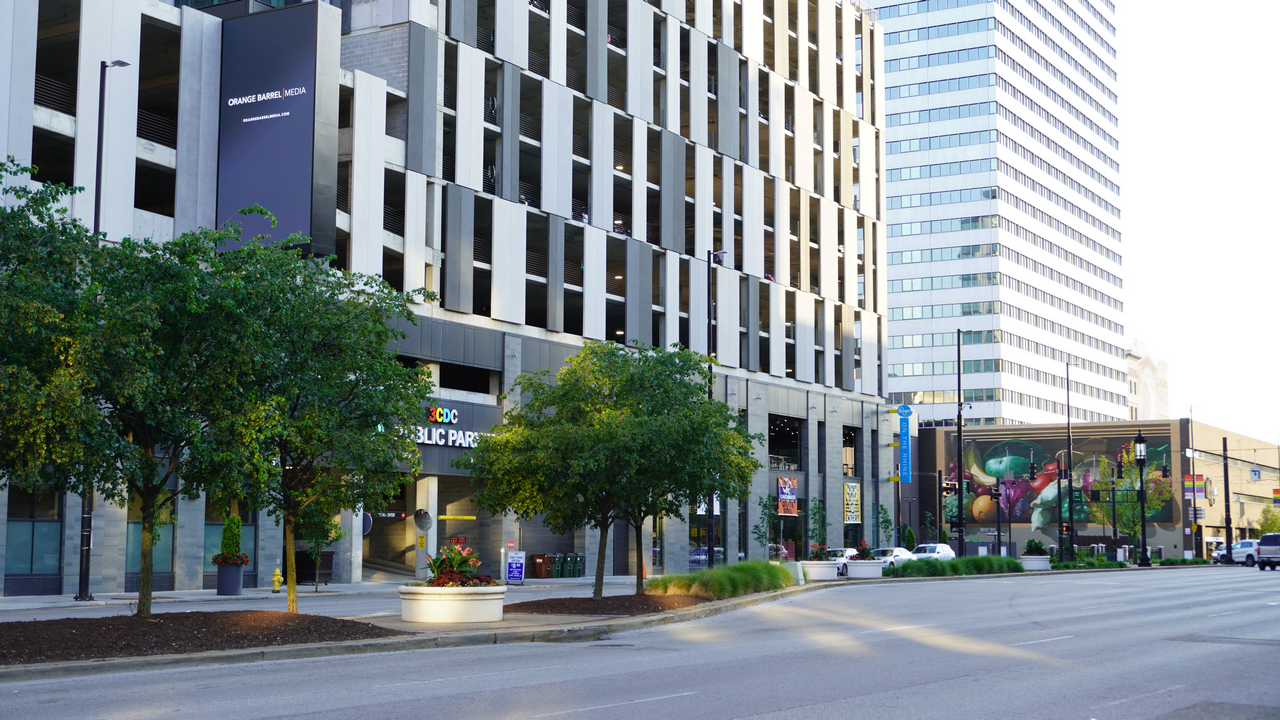 City street with modern buildings, trees, and a mural.