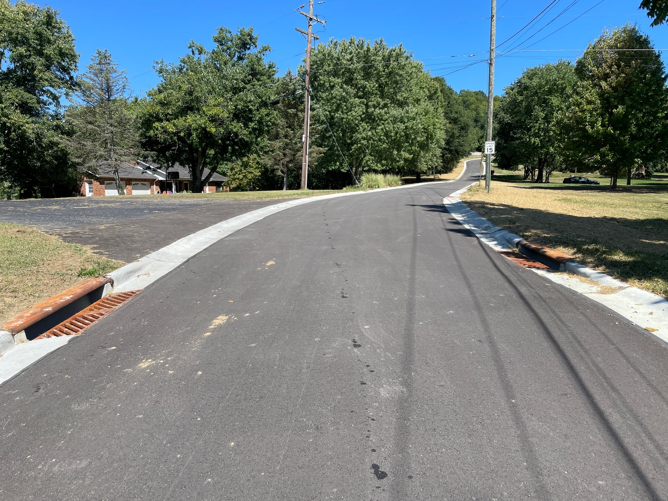 Paved road with green trees and a clear blue sky.