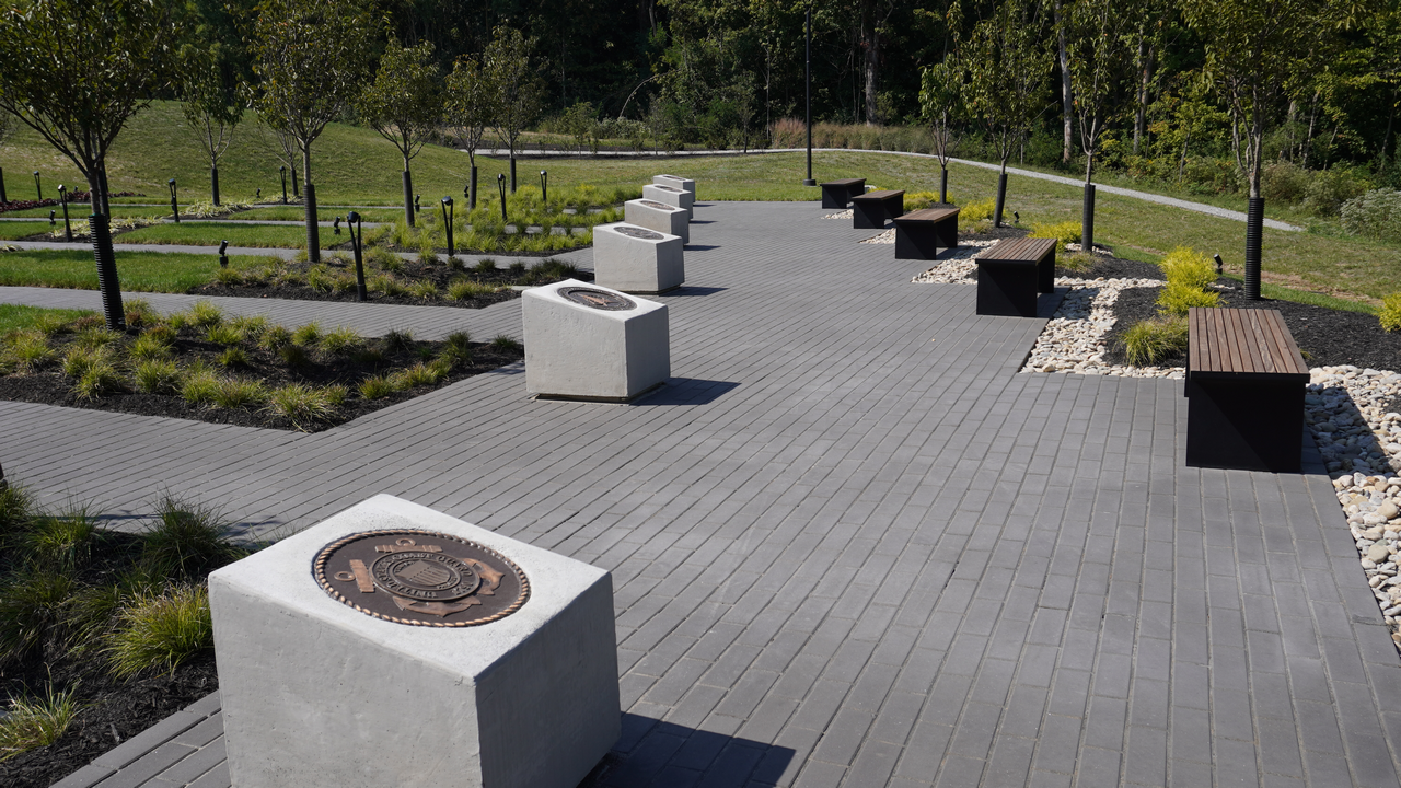 Walkway with memorial plaques on raised platforms, surrounded by trees and greenery.