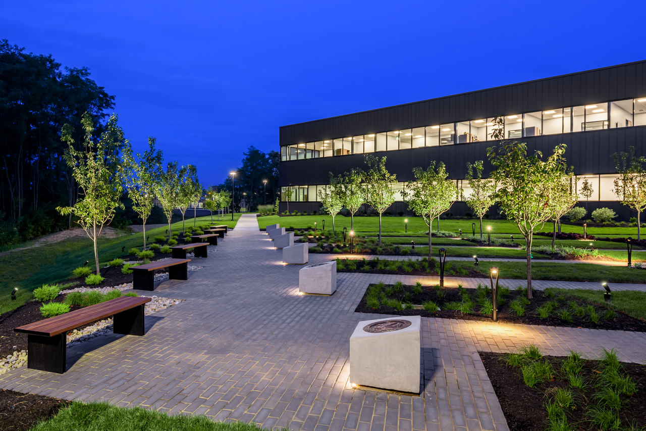 Walkway and garden beside a lit modern building at dusk.