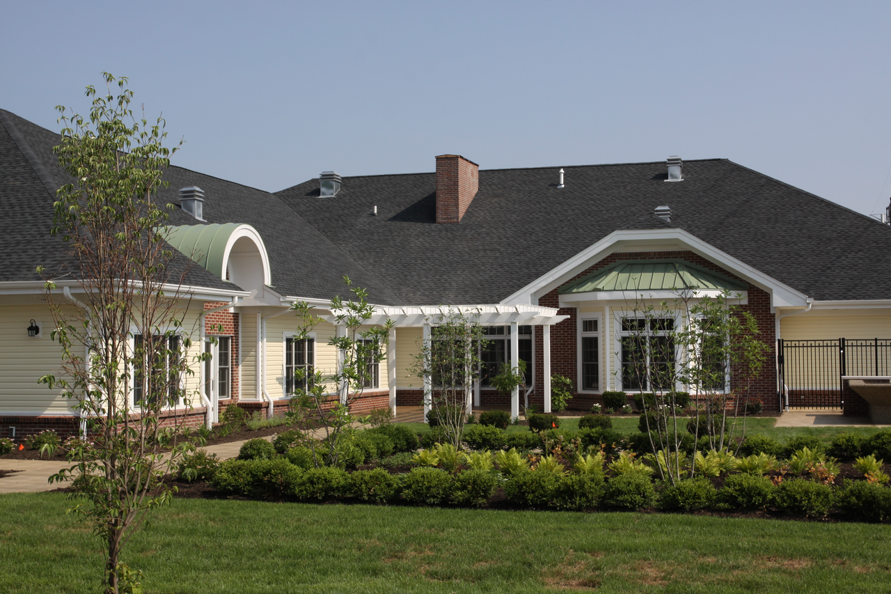 A white and brick house with a black roof, green lawn, and shrubs.