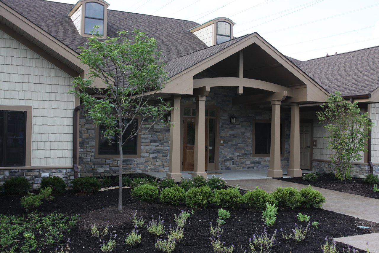 Stone house entrance with columns, shrubs, and two small trees.