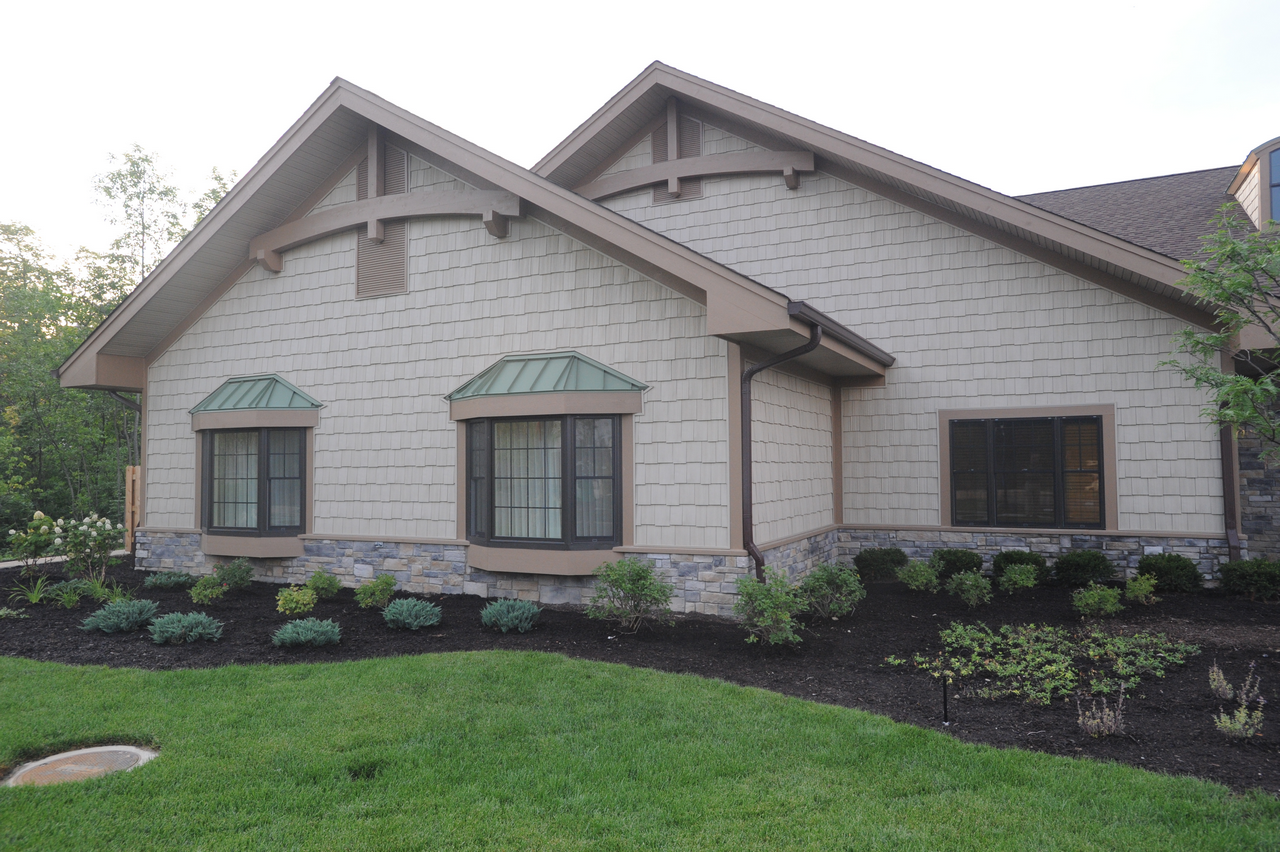 House with stone and siding exterior, surrounded by lush landscaping.