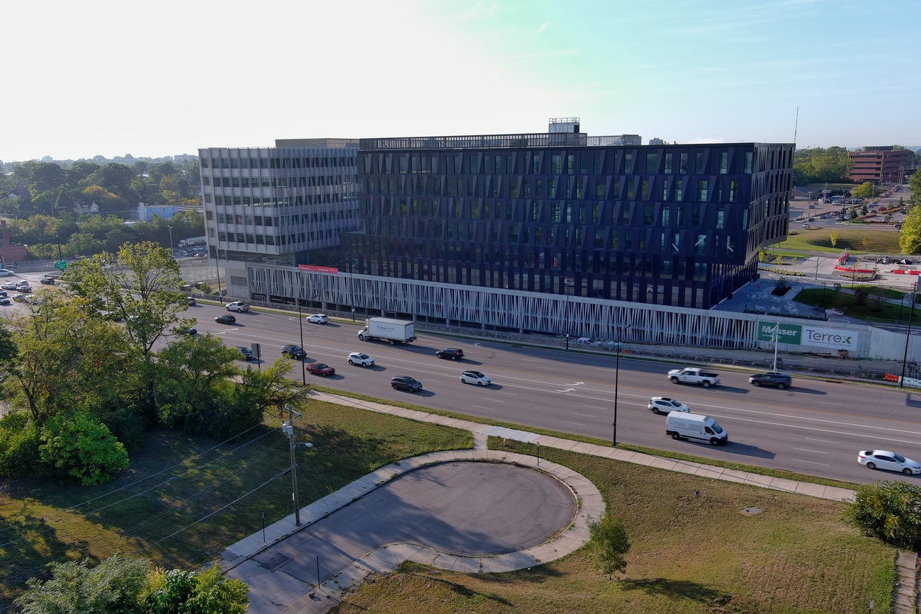 Aerial view of a large black building beside a highway with moving cars.