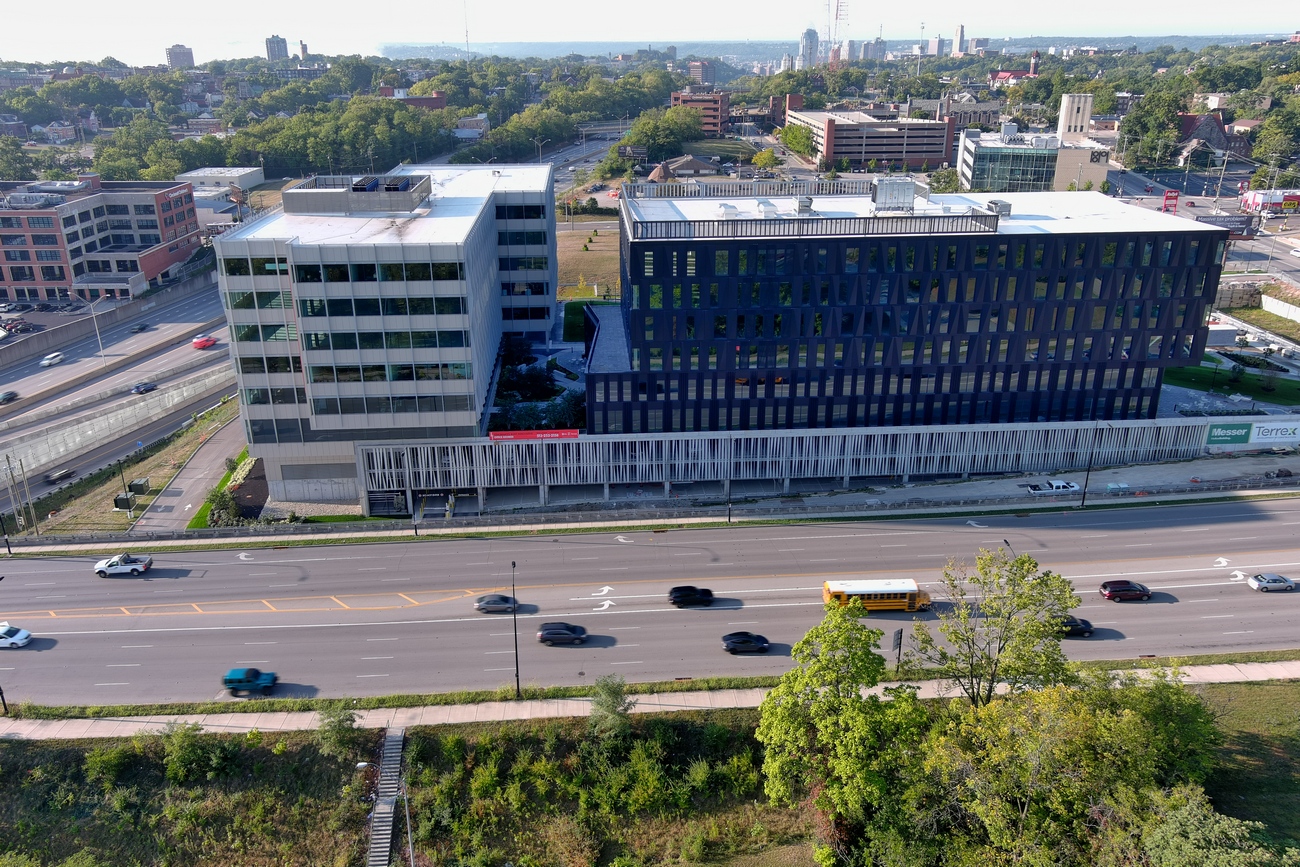 Aerial view of a modern office building near a highway, with cars and greenery.