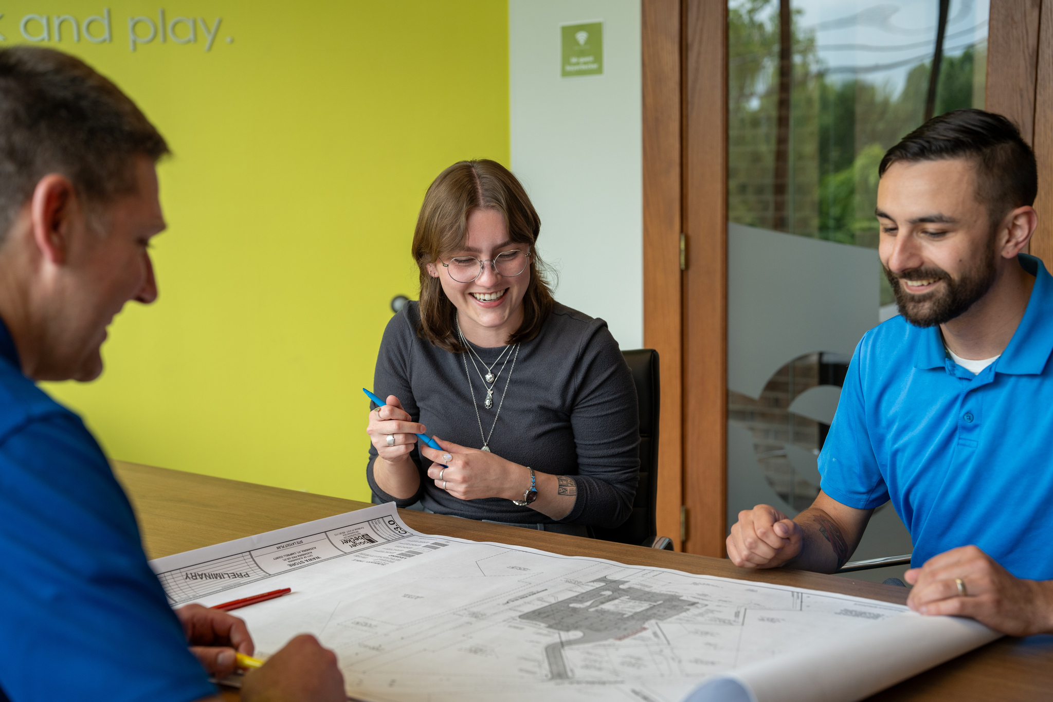 Three people smiling and discussing a large paper map at a table.