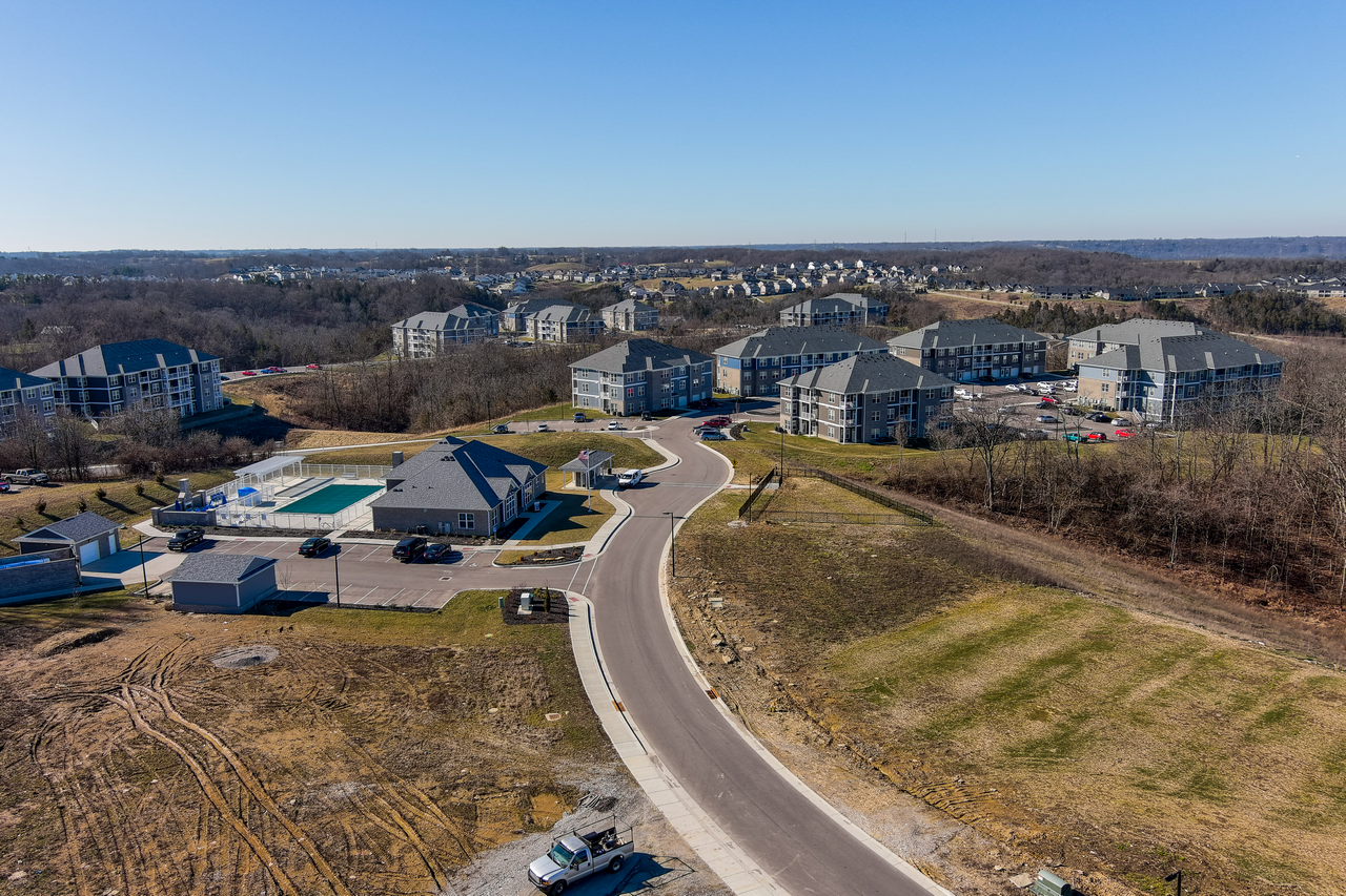 Aerial view of a suburban neighborhood with houses and a pool under a clear blue sky.