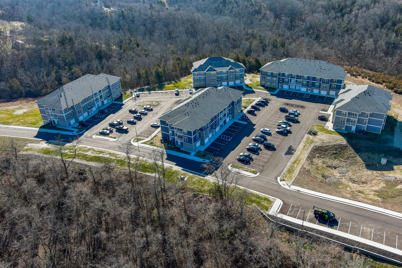 Aerial view of apartment complex surrounded by trees and parking lots.