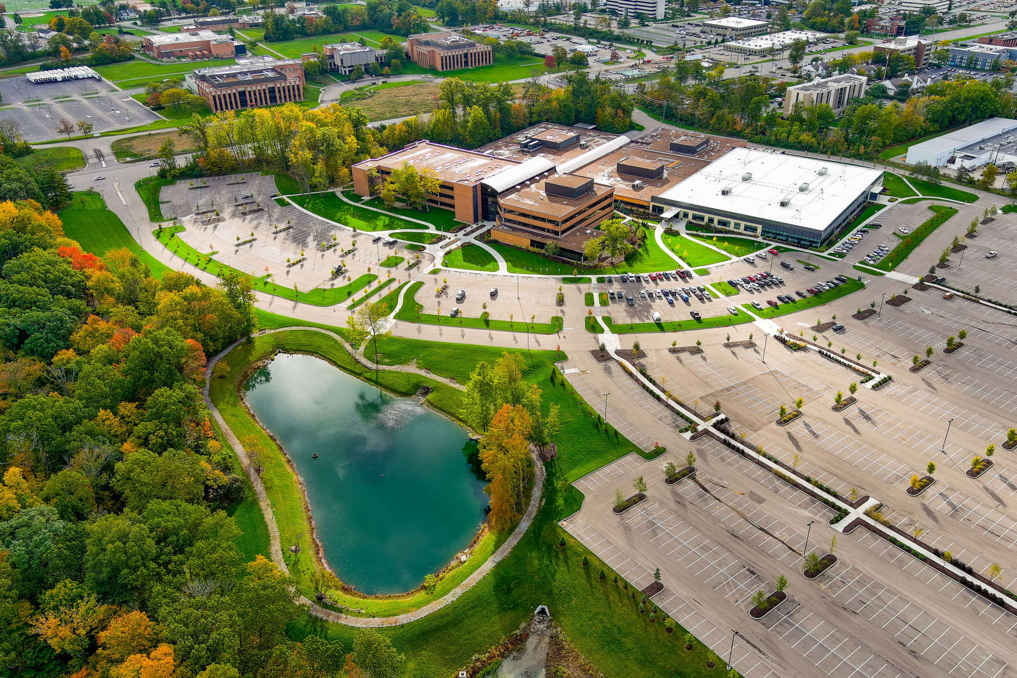 Aerial view of a campus with buildings, parking lot, and a small pond surrounded by trees.