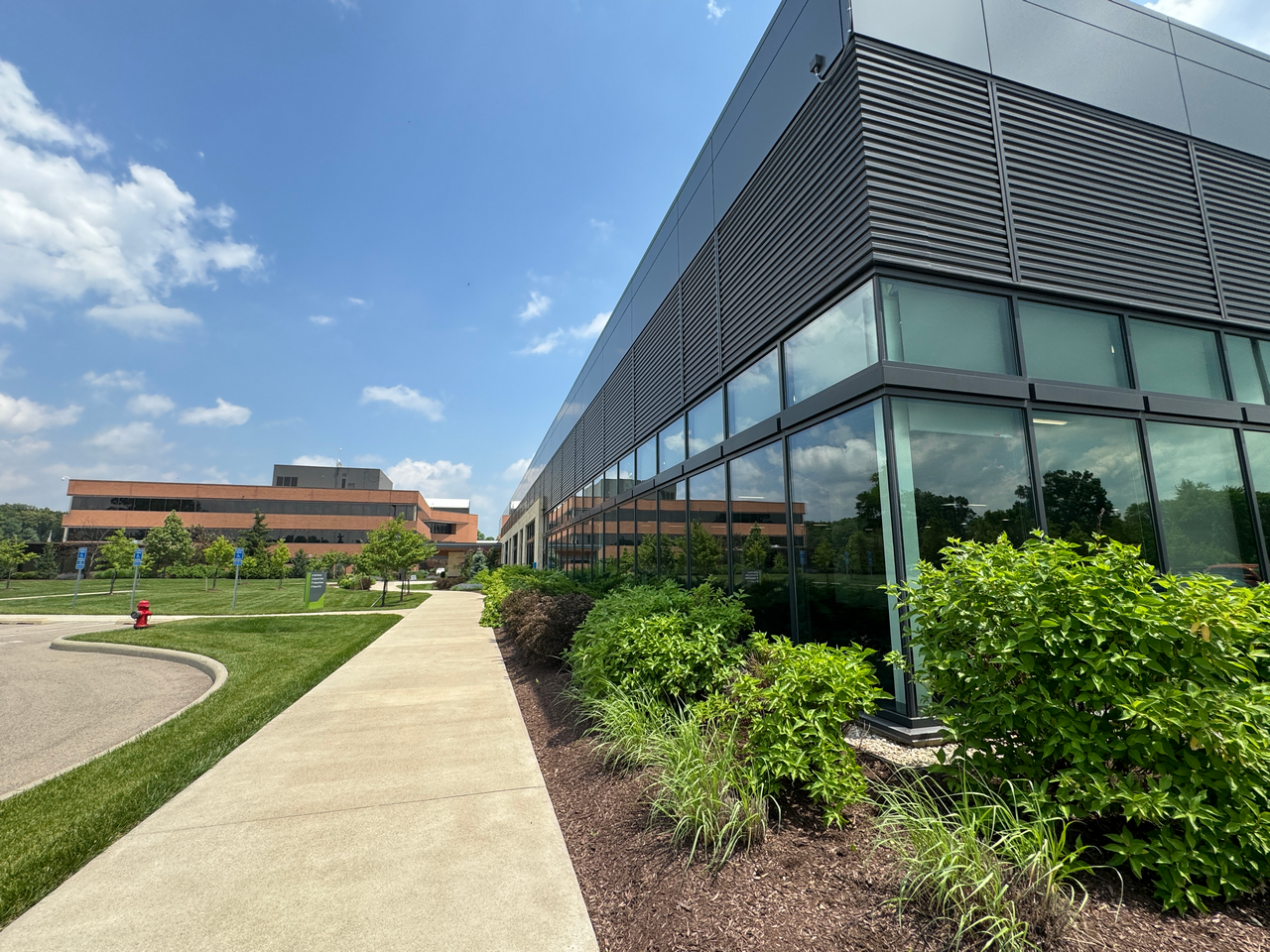 Modern glass building with sidewalk and greenery on a sunny day.