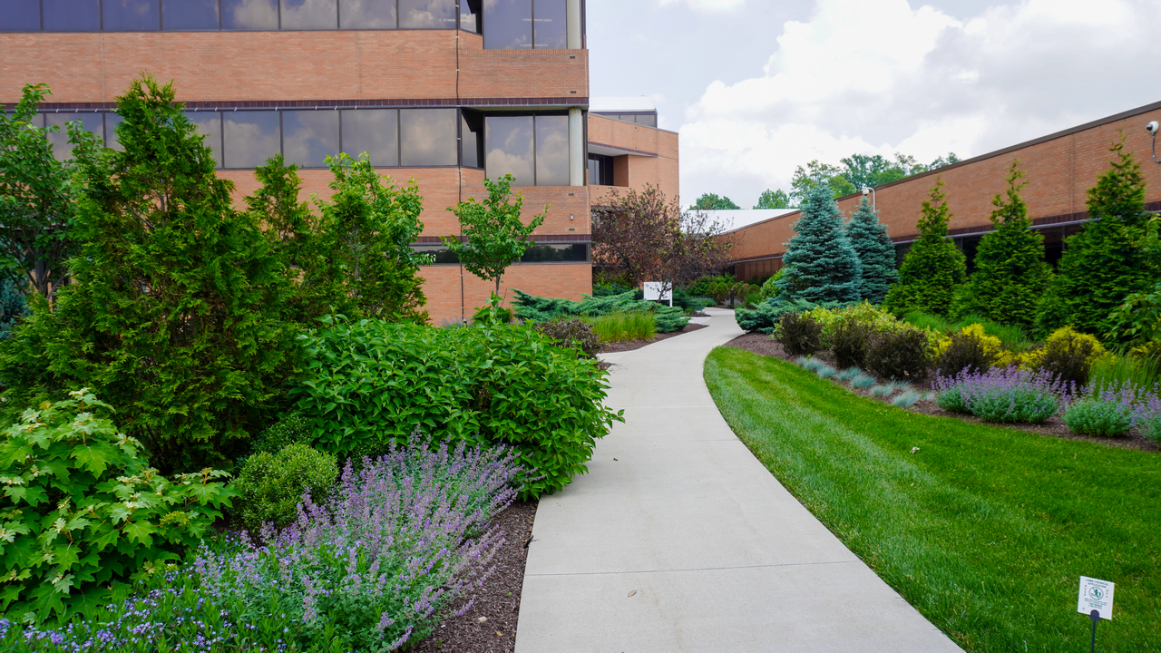 Pathway through lush gardens beside a brick building on a cloudy day.