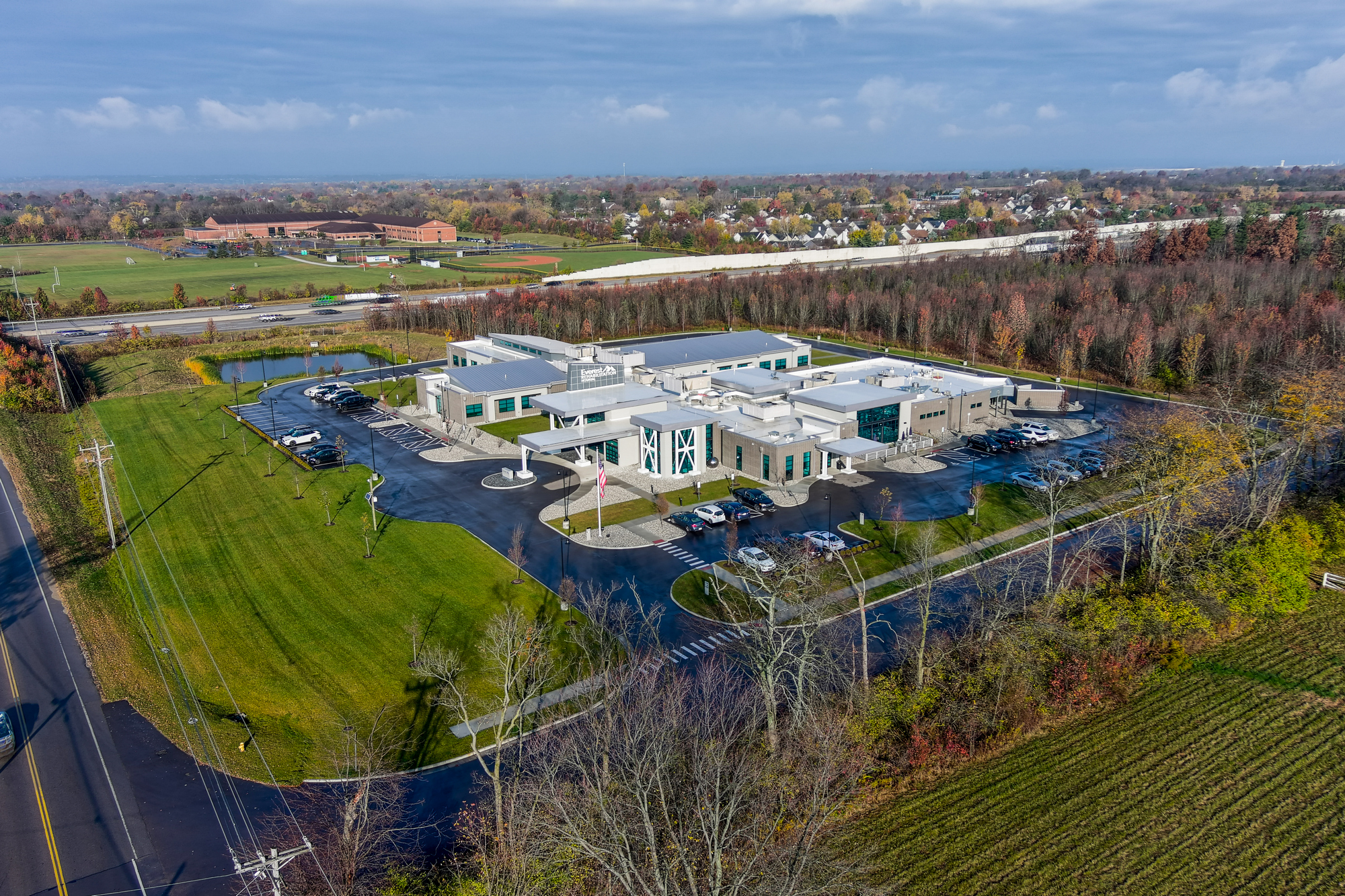 Aerial view of a modern building surrounded by fields and roads on a clear day.