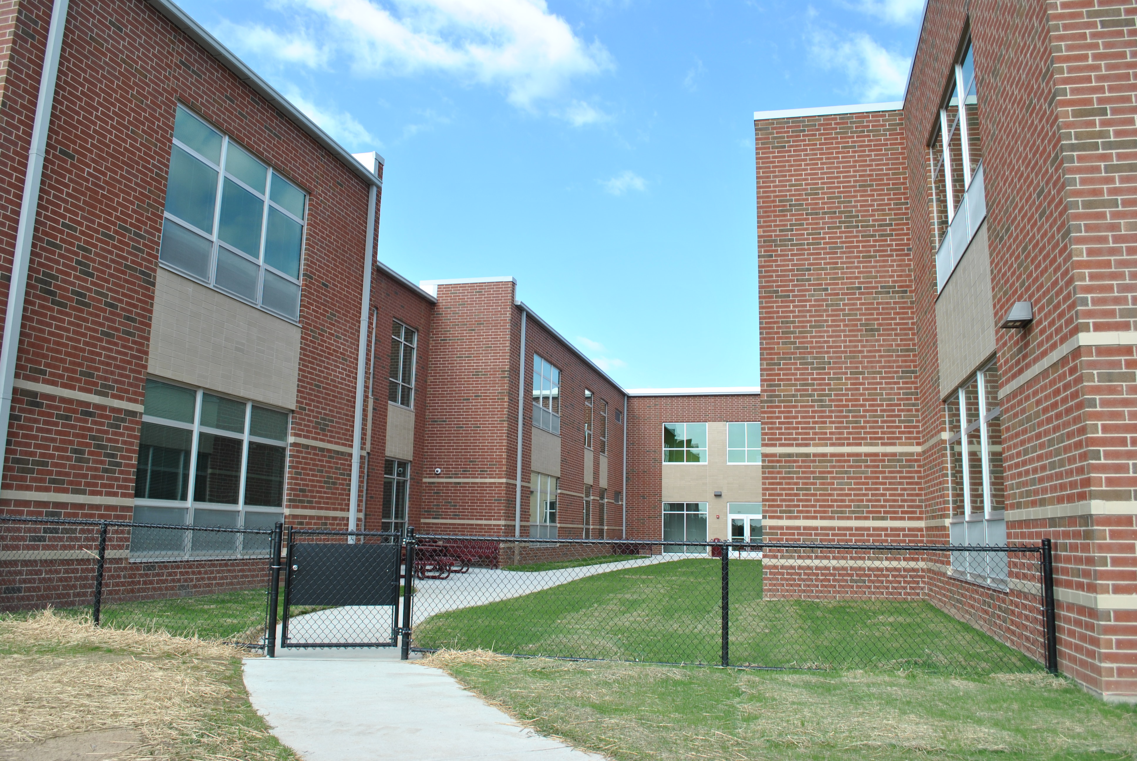 Red brick school building with grassy courtyard and paved walkway under a blue sky.
