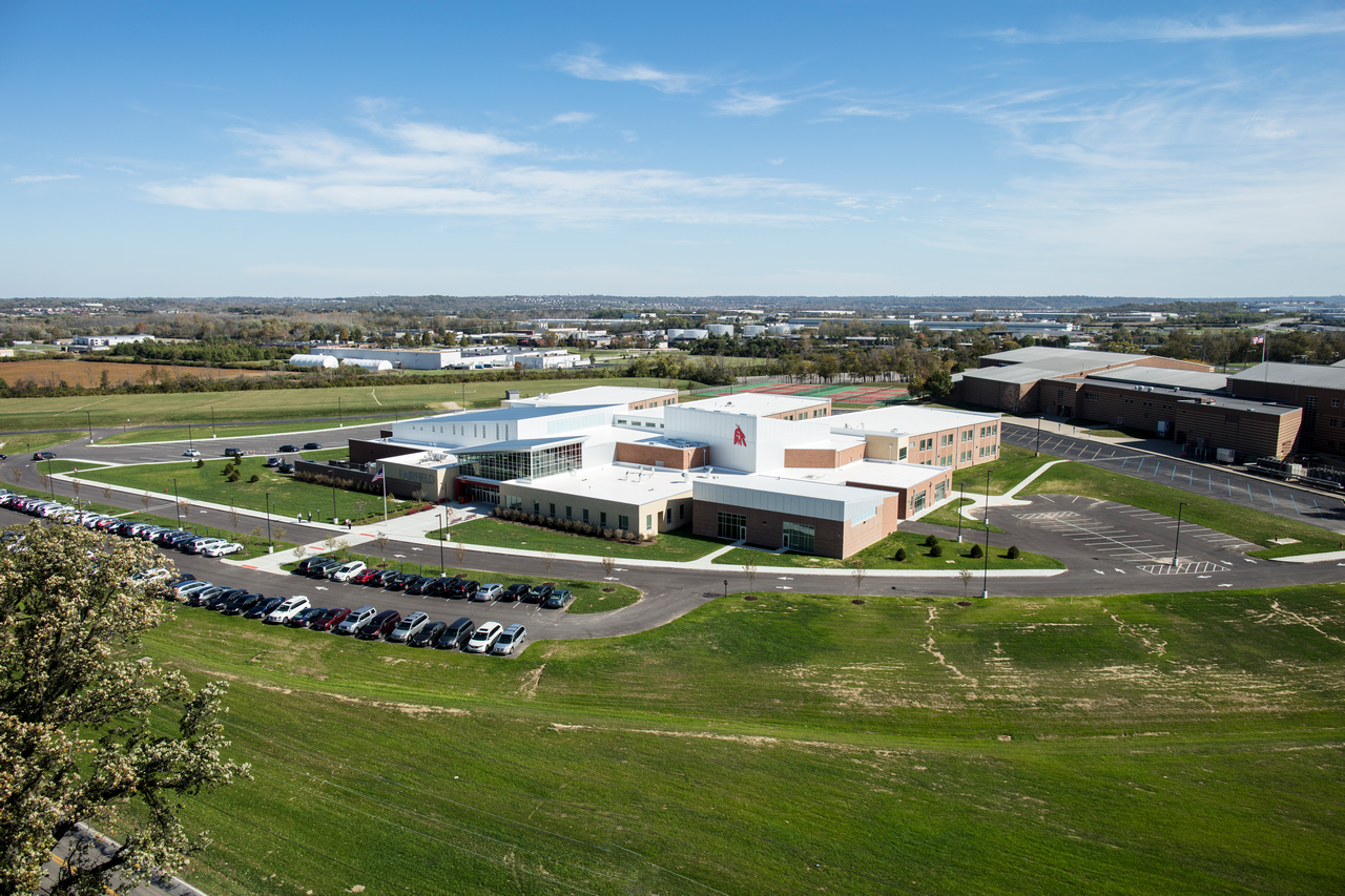 Aerial view of a large building complex with parking, surrounded by green fields.