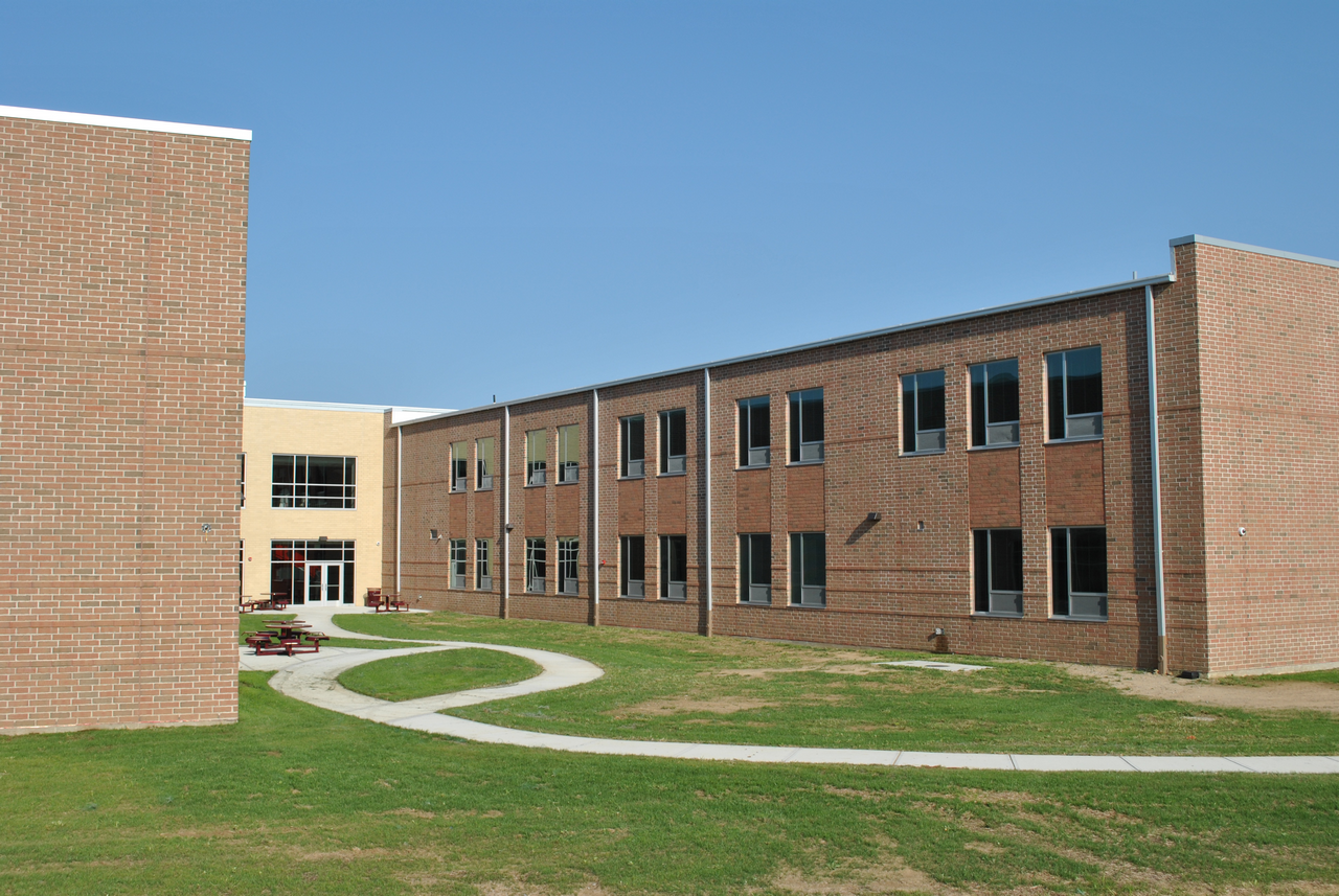 Brick school building with two stories, clear sky, and green lawn.