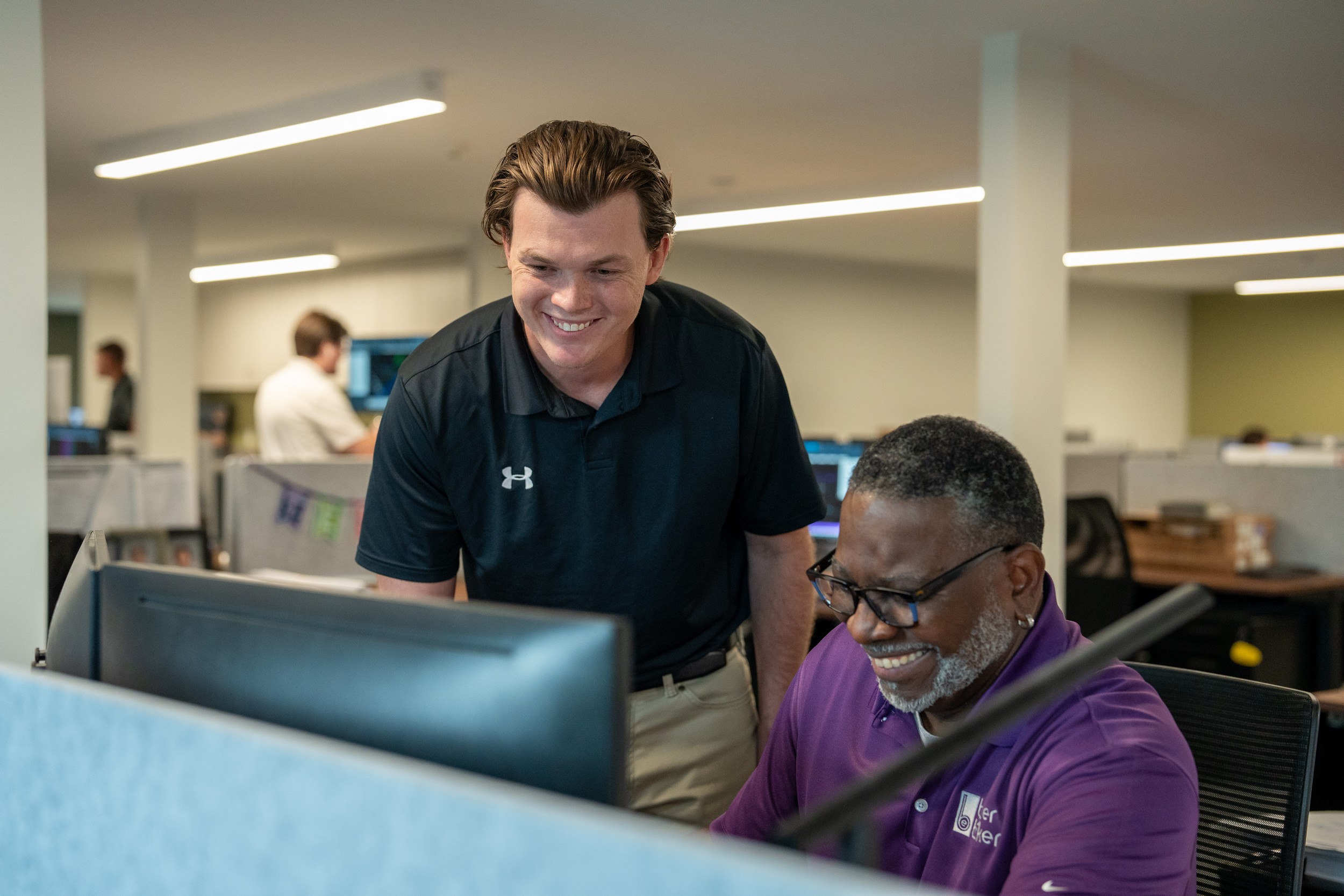 Two colleagues smiling at a computer in an office.