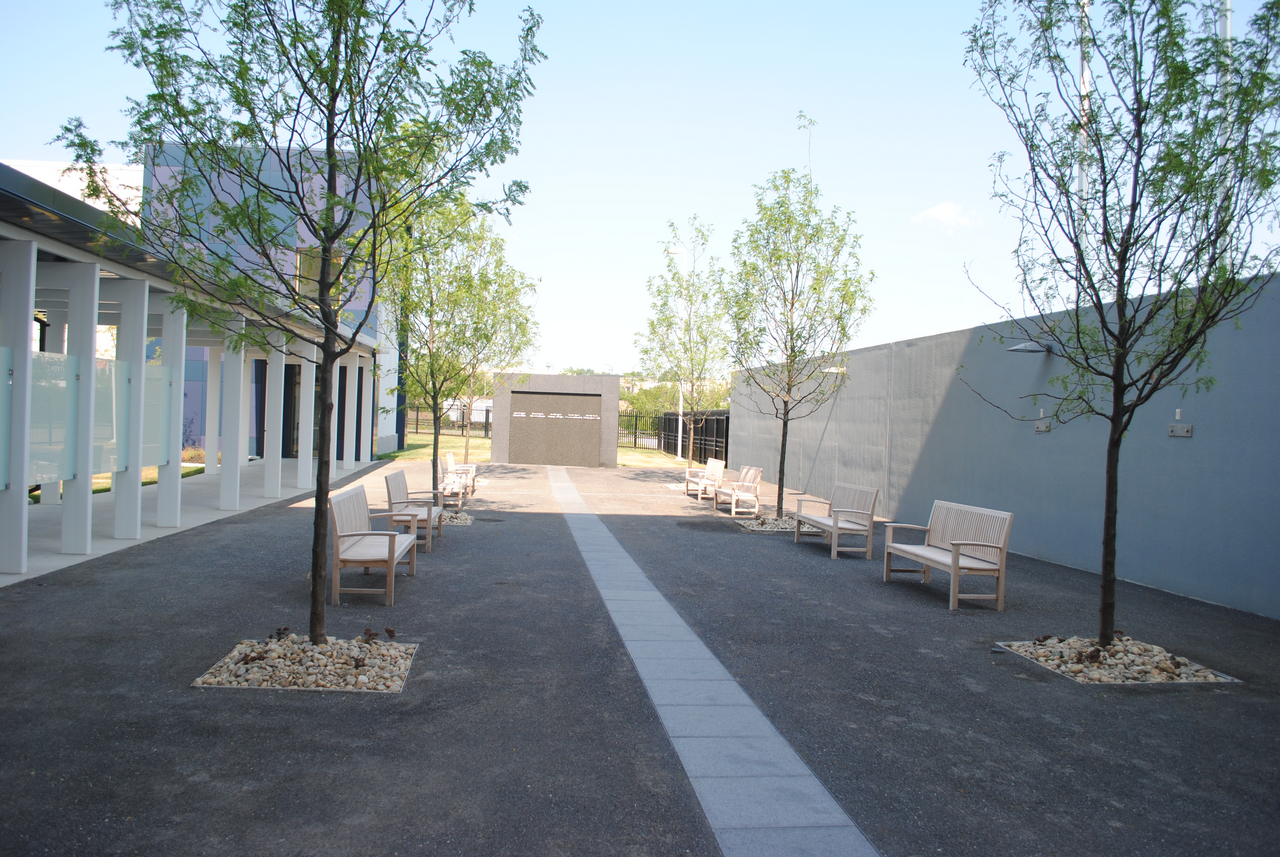 Modern courtyard with trees, benches, and a pathway under clear skies.