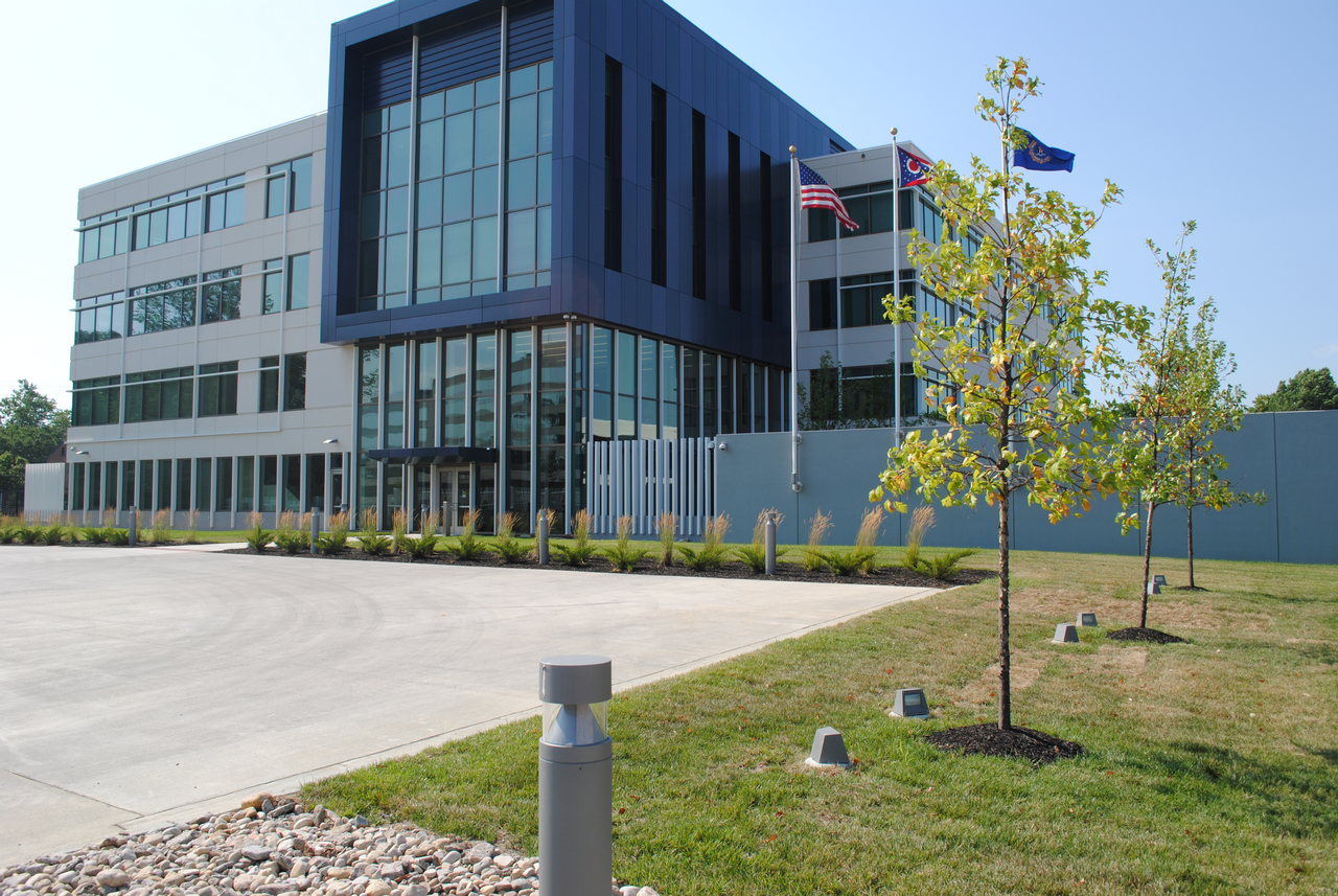 Modern office building with glass facade, small trees, and flagpoles outside.
