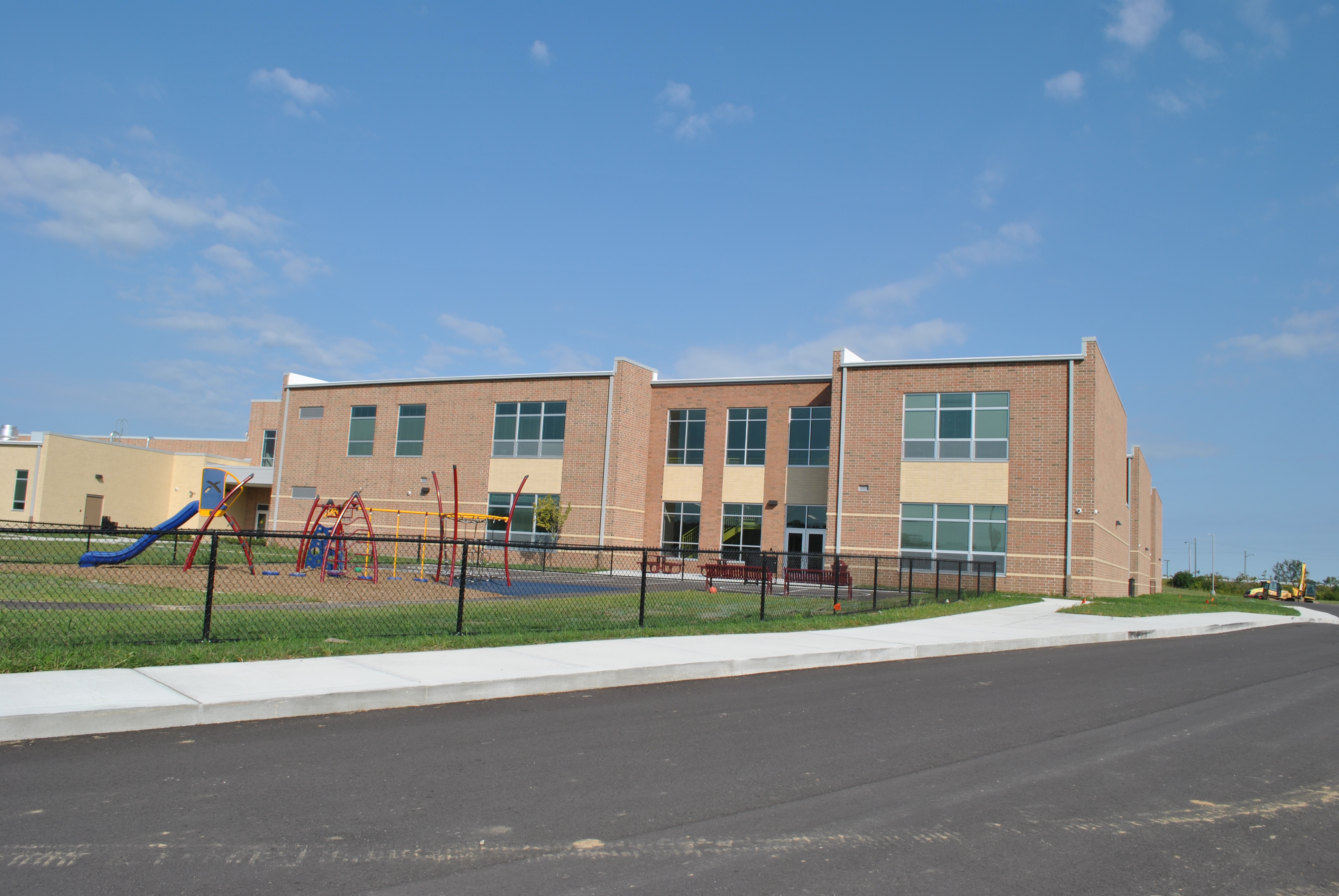 Red brick school building with a playground under a clear blue sky.