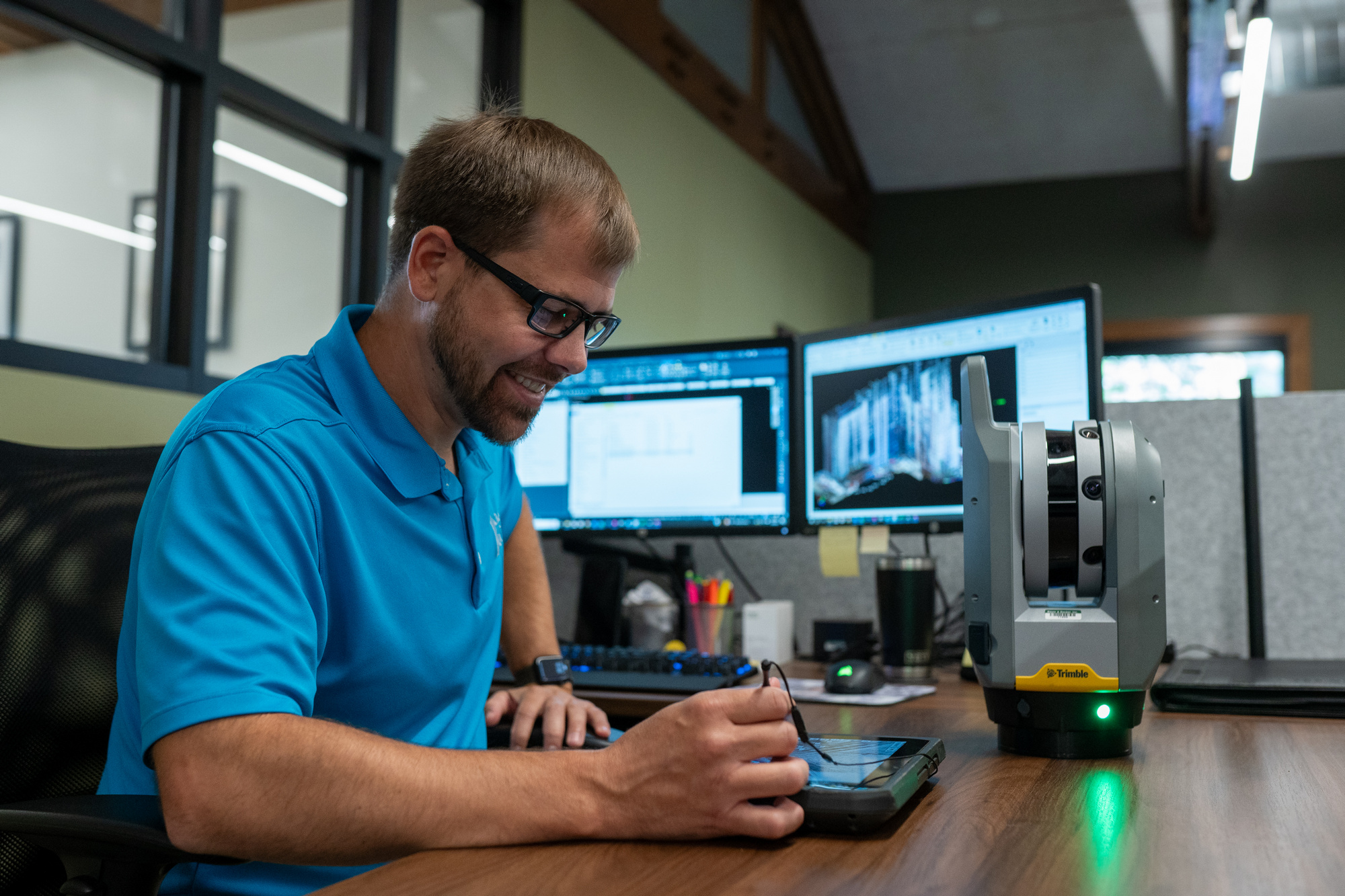 Man in a blue shirt works at a desk with dual monitors.
