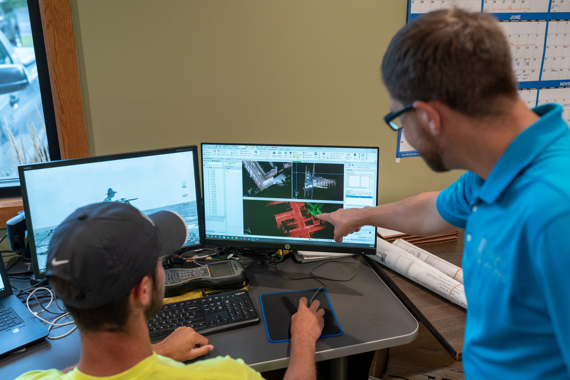 Two men working at a desk with dual computer monitors.