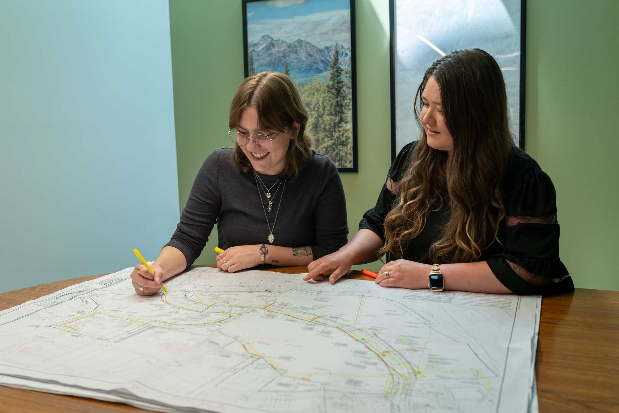 Two women smiling and marking a large map on a table.