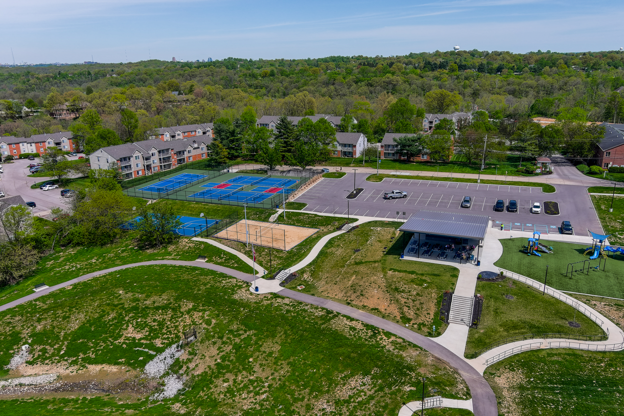 Aerial view of a park with sports courts, parking lot, and trees under a blue sky.
