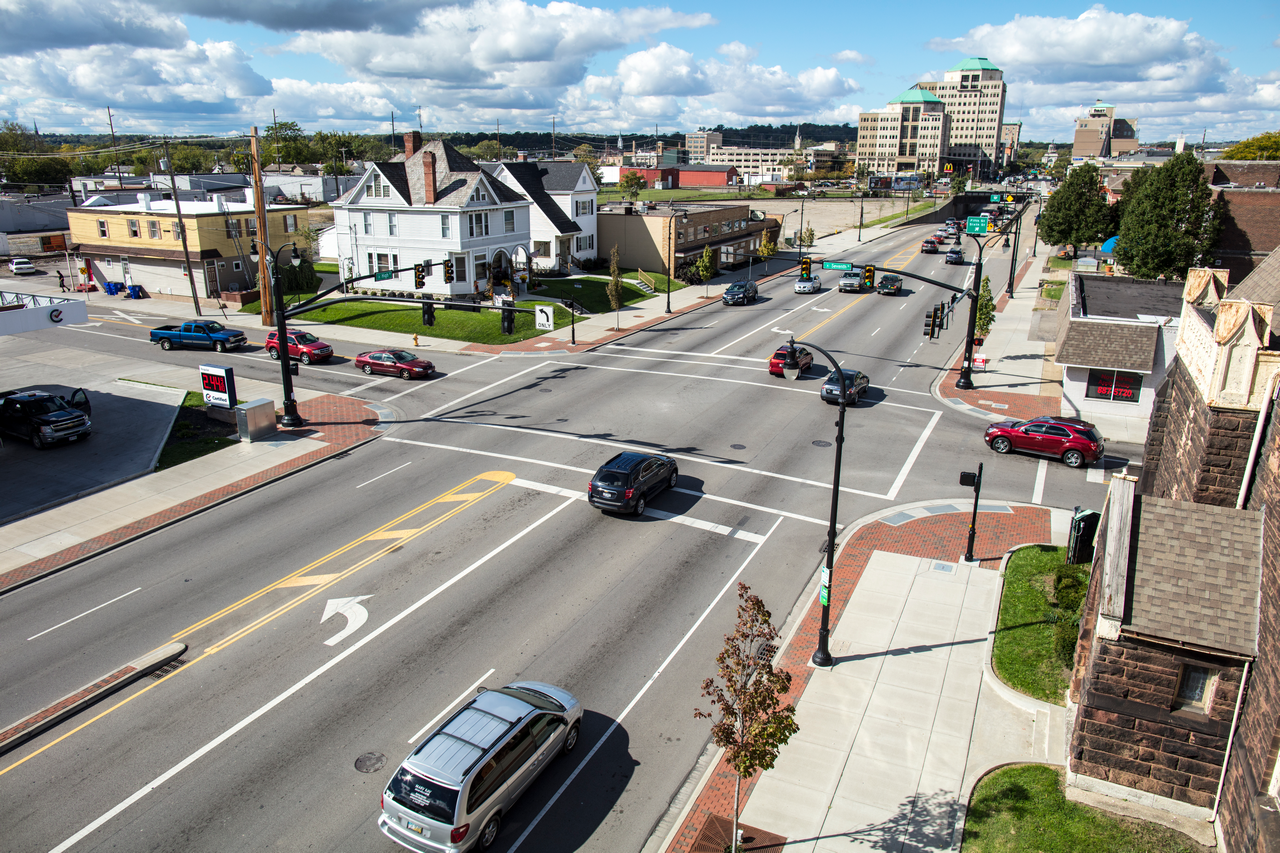 Busy urban intersection with cars, buildings, and a cloudy sky.