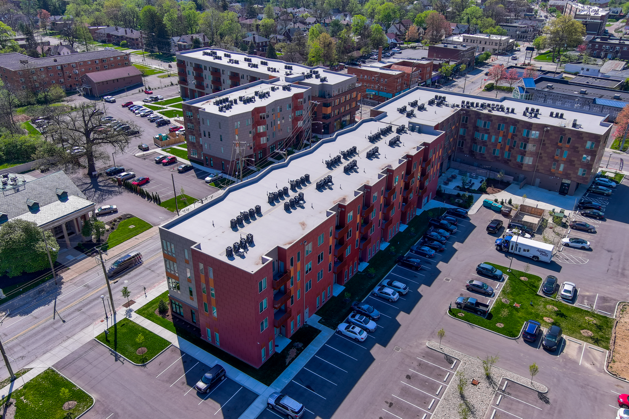 Aerial view of a red-brick apartment complex with parking lot and trees nearby.