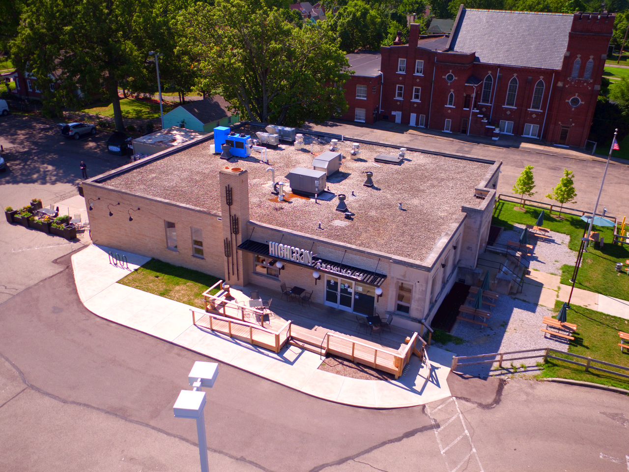 Aerial view of a beige building with a patio, surrounded by trees and a road.