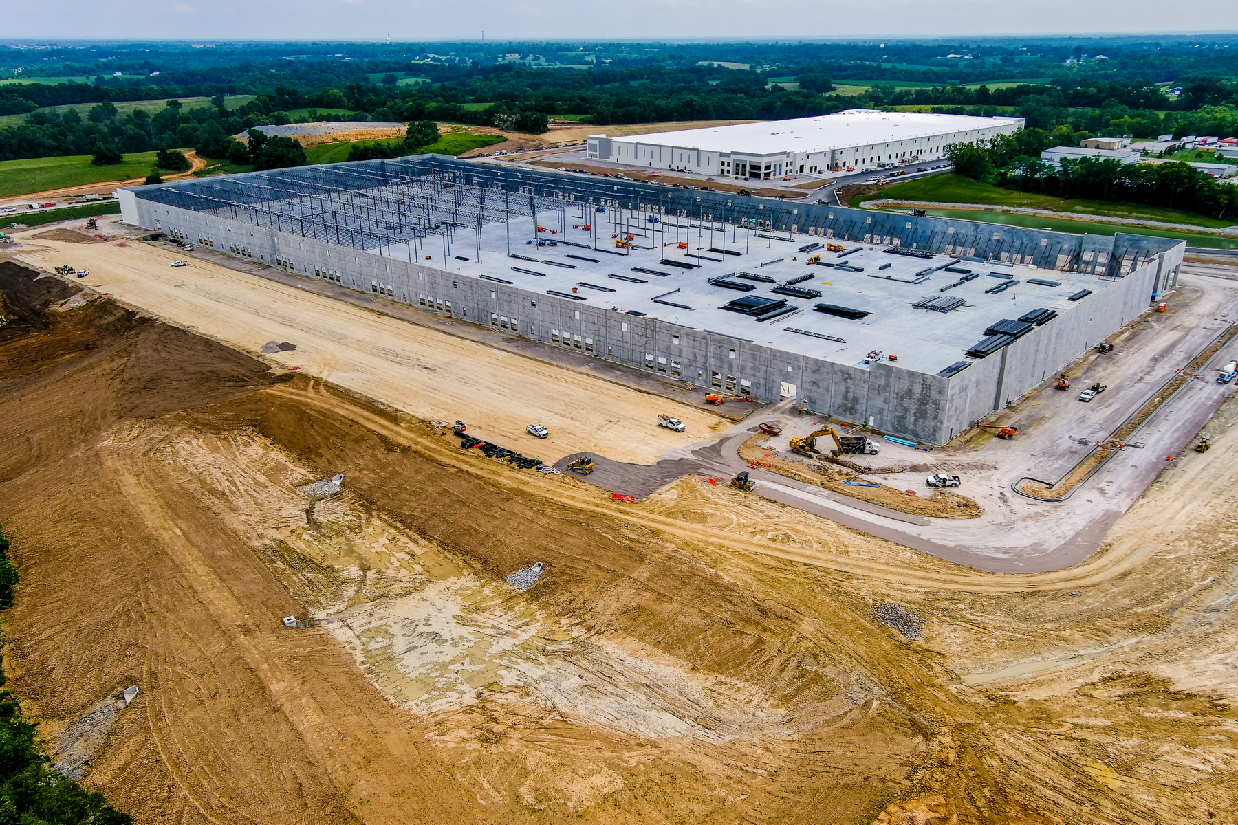 Construction site of a large warehouse with surrounding fields and machinery.