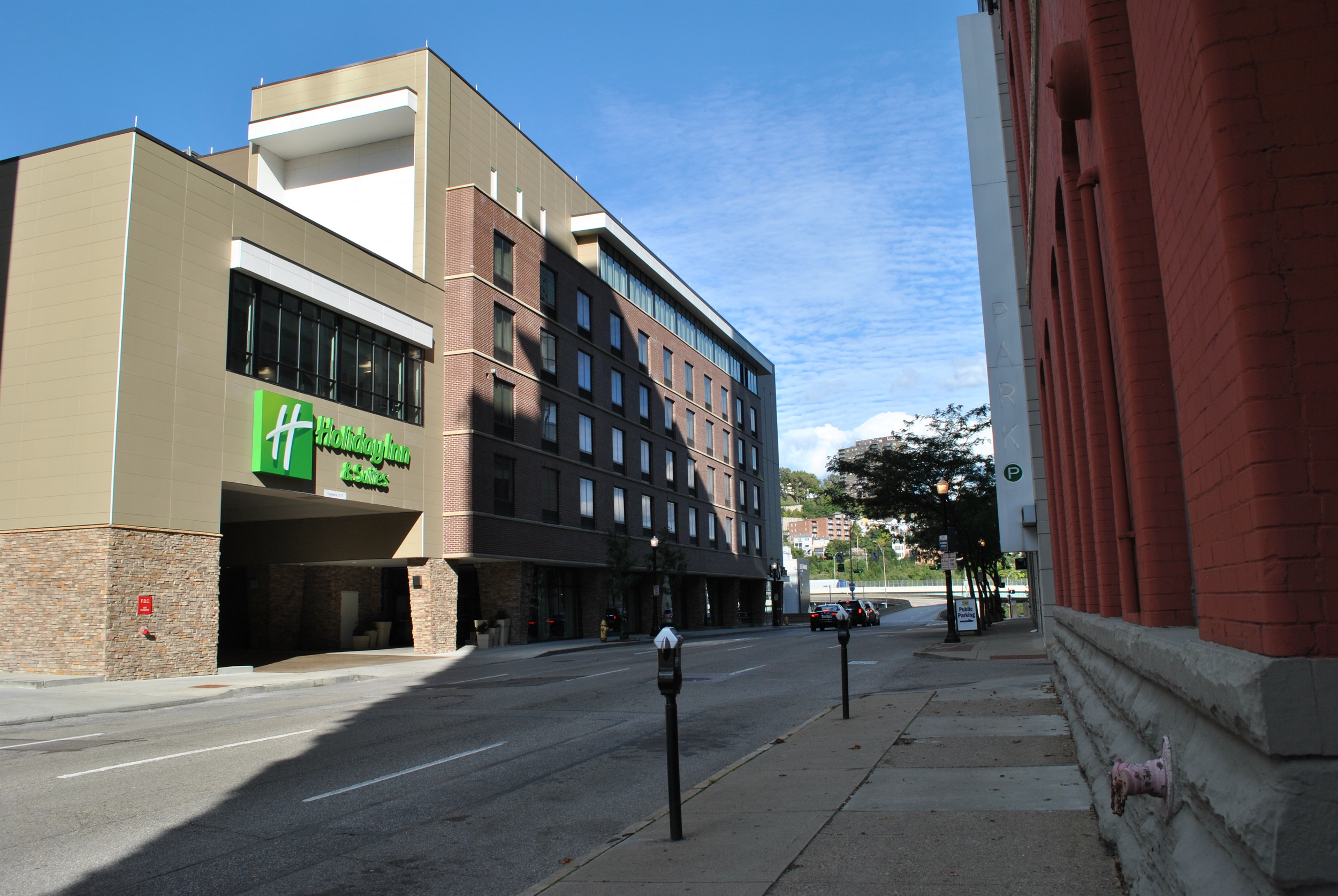 Street view with a multi-story hotel and a brick building, under a clear blue sky.