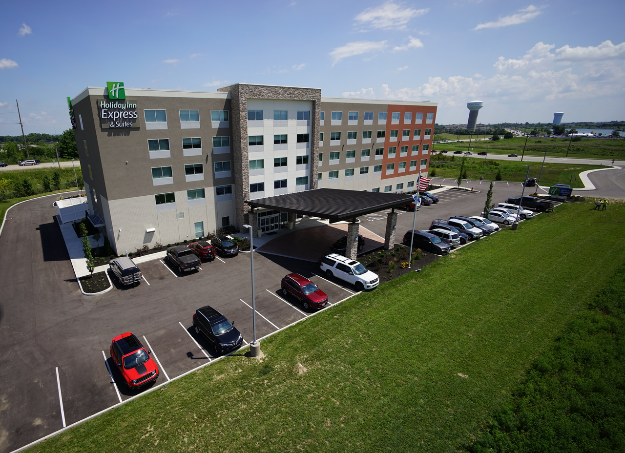 Modern hotel with parking lot, surrounded by green grass, under a blue sky.