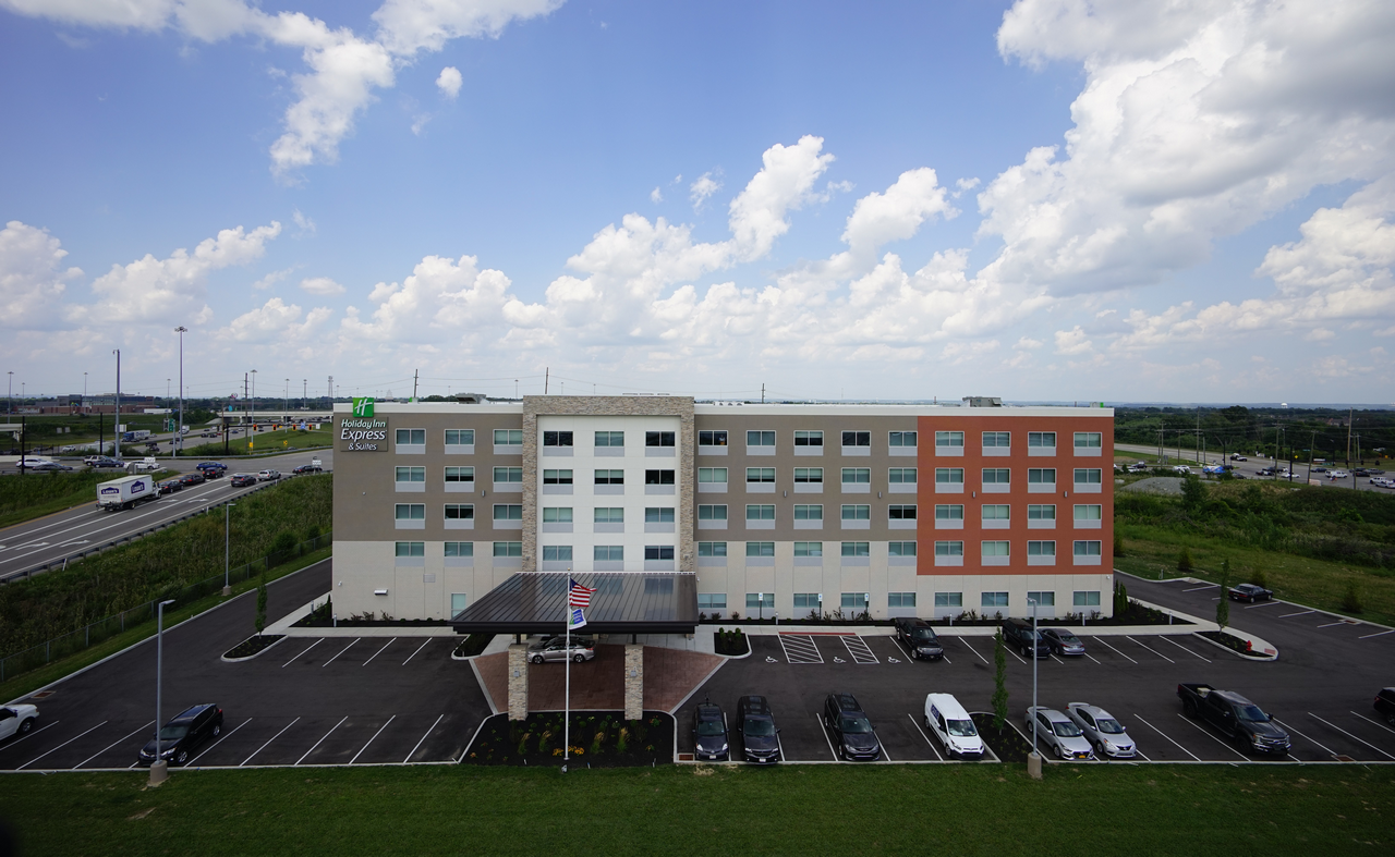 Four-story hotel building with parking lot and cloudy sky.