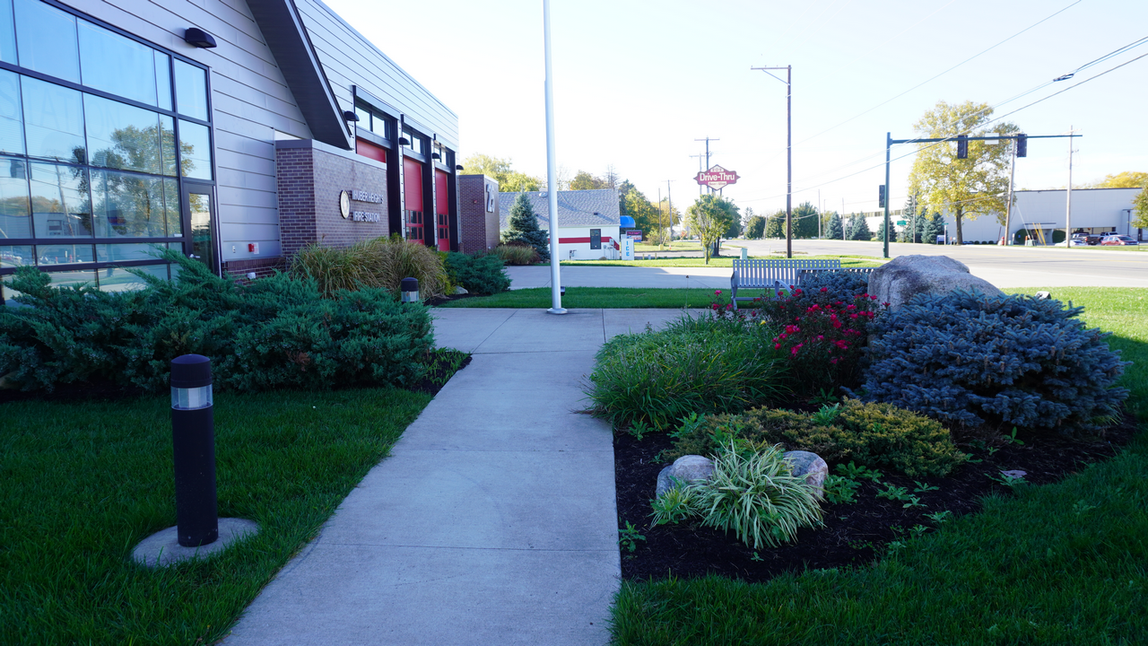 Pathway with green lawn and shrubs beside a building, street visible.