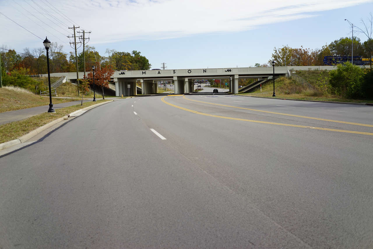 Wide, empty road leading to an overpass under a blue sky.