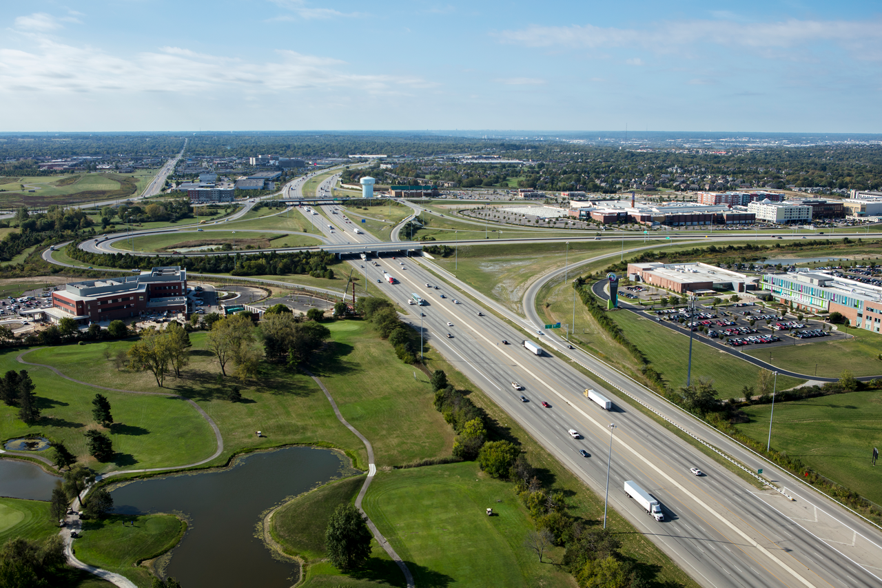 Aerial view of a highway intersection with surrounding green spaces and buildings.