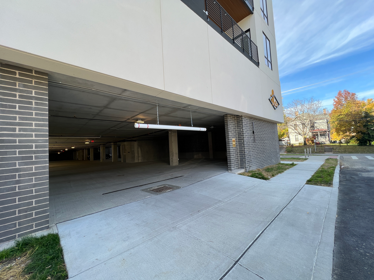 Building entrance with parking garage and sidewalk, trees in background.