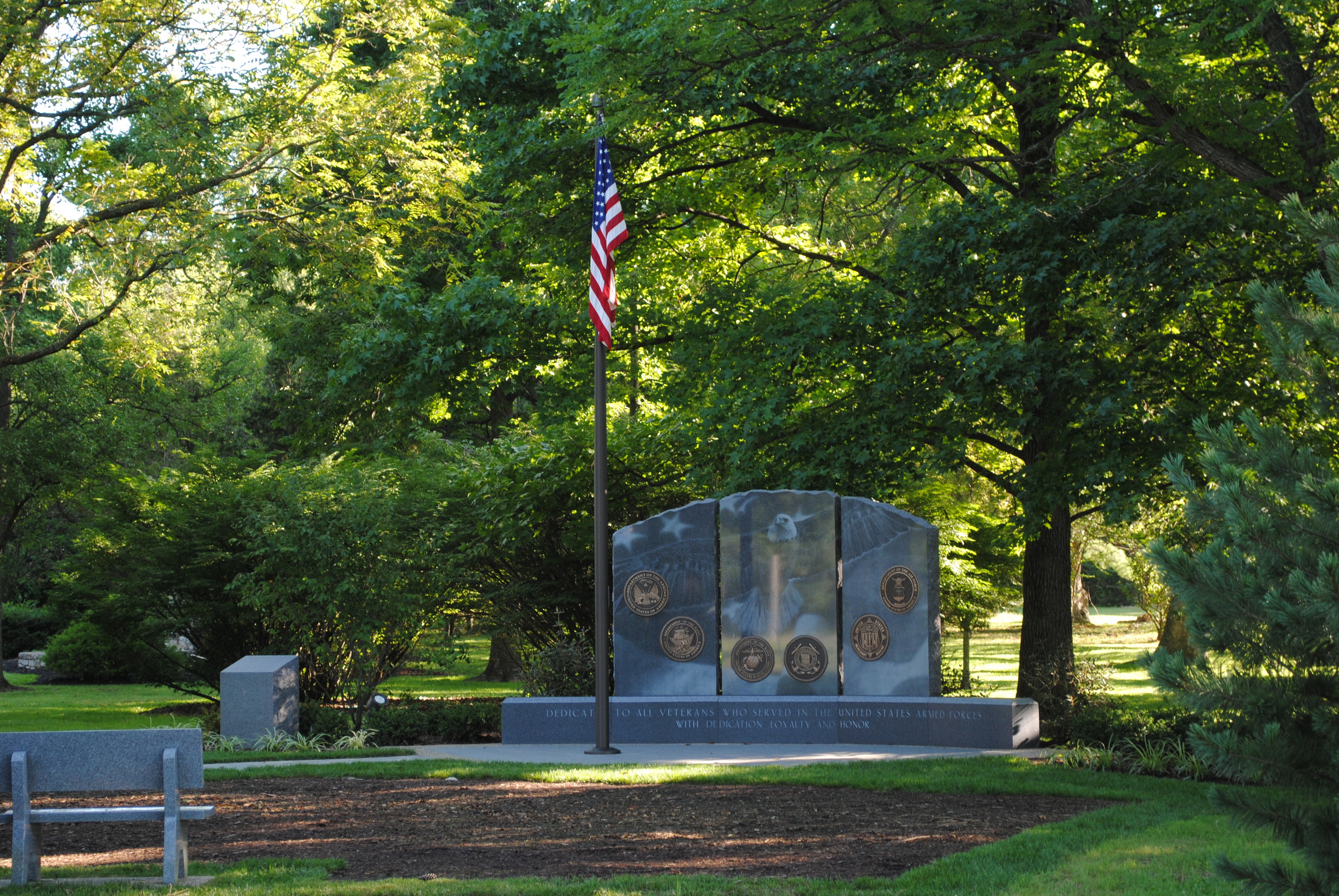 Memorial stone with flagpole in a serene, tree-filled park.