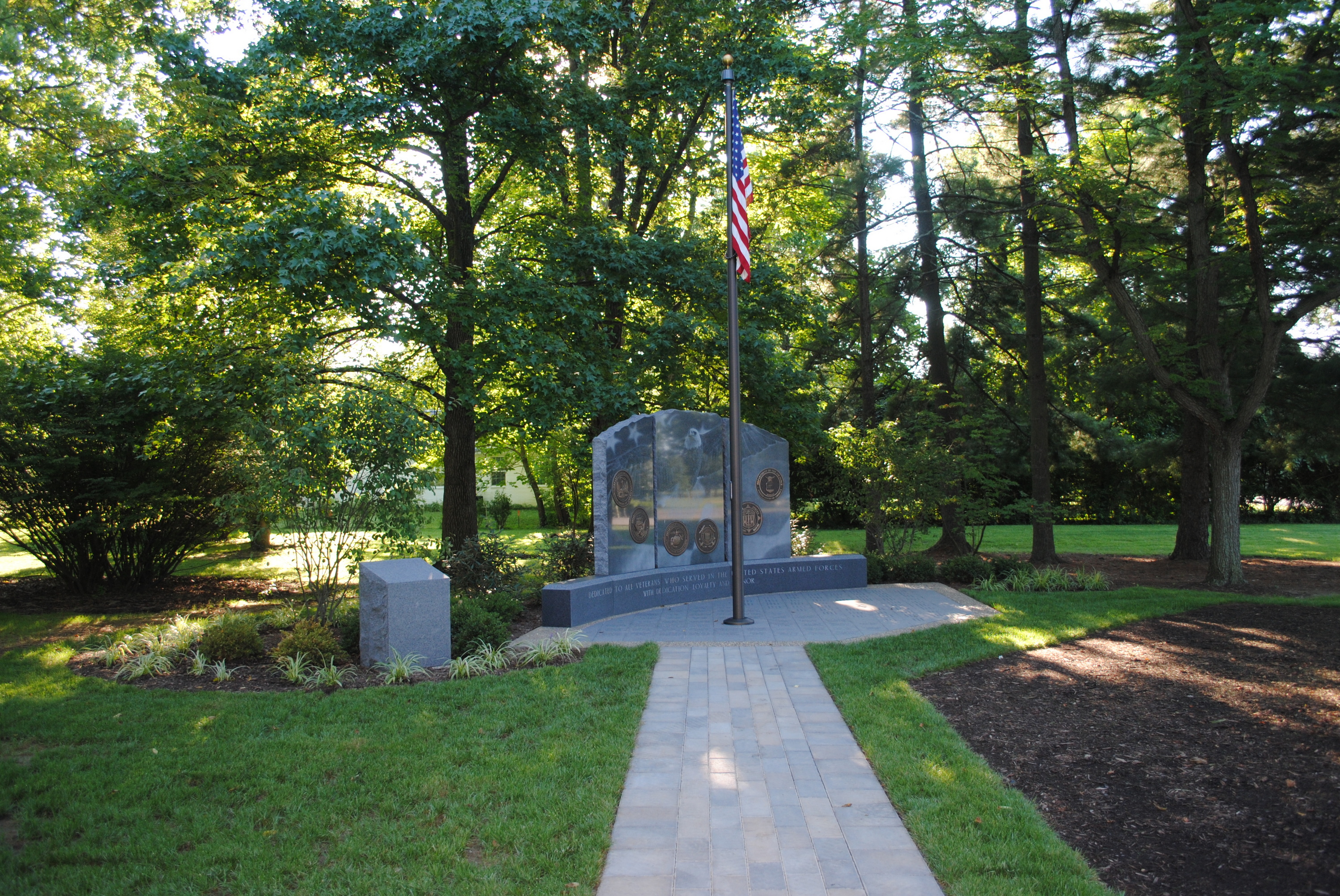 Pathway leading to a stone memorial in a park, surrounded by trees and greenery.