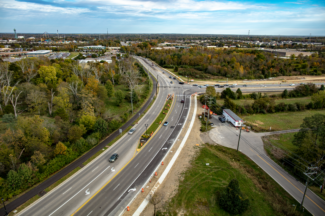 Aerial view of a highway through forested and industrial areas under a blue sky.