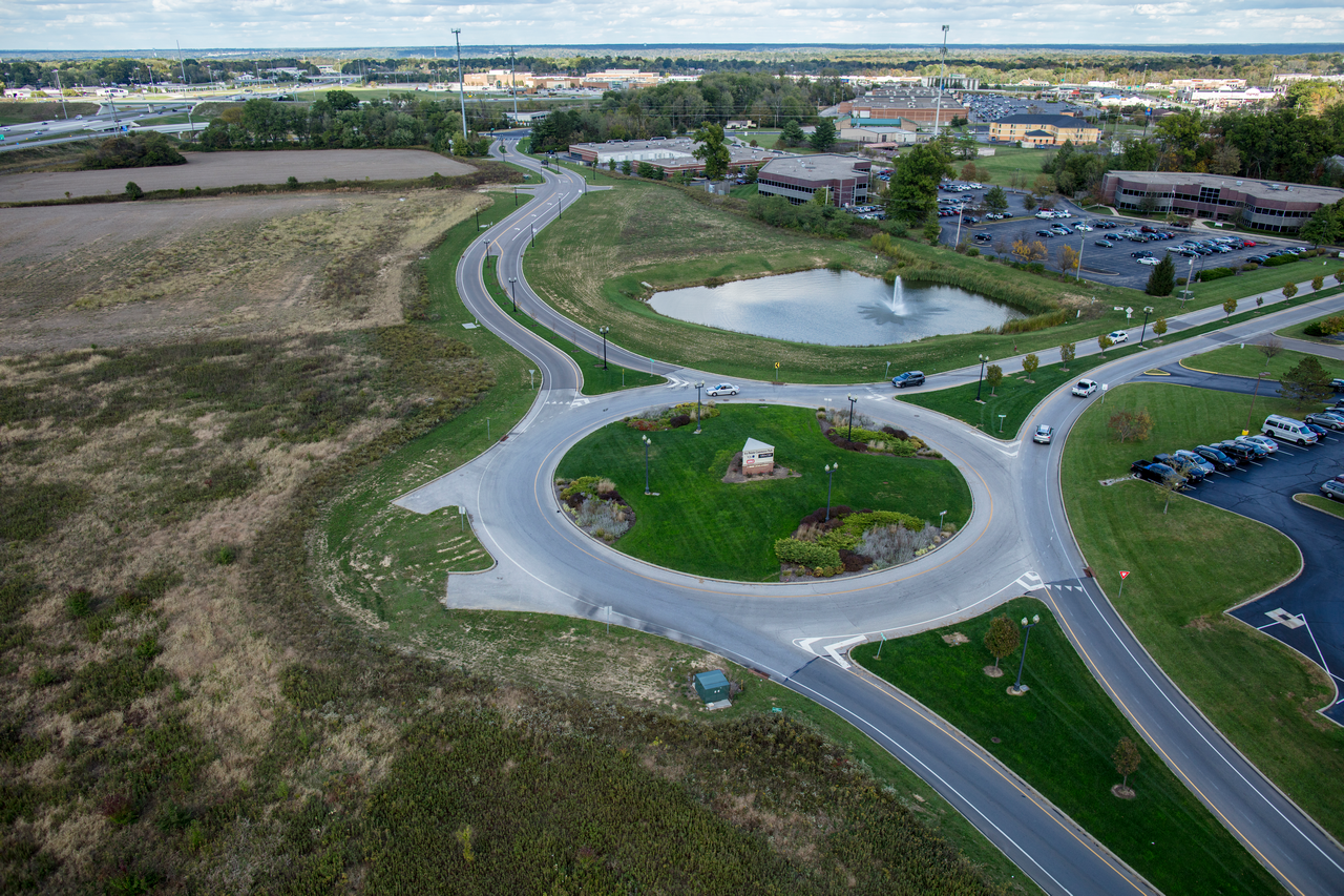 Roundabout with green center, surrounded by roads and grassy fields.
