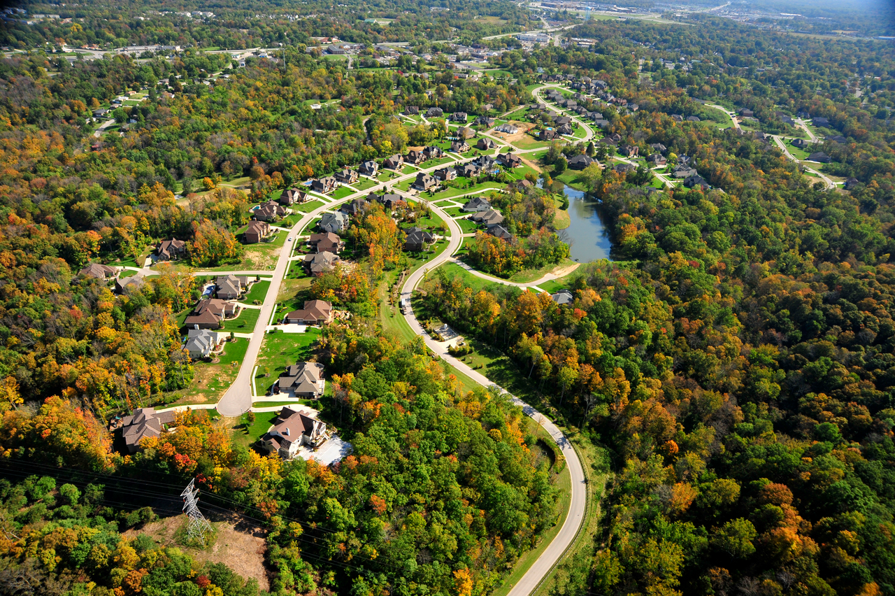 Aerial view of a curving road through a forested residential area in autumn.