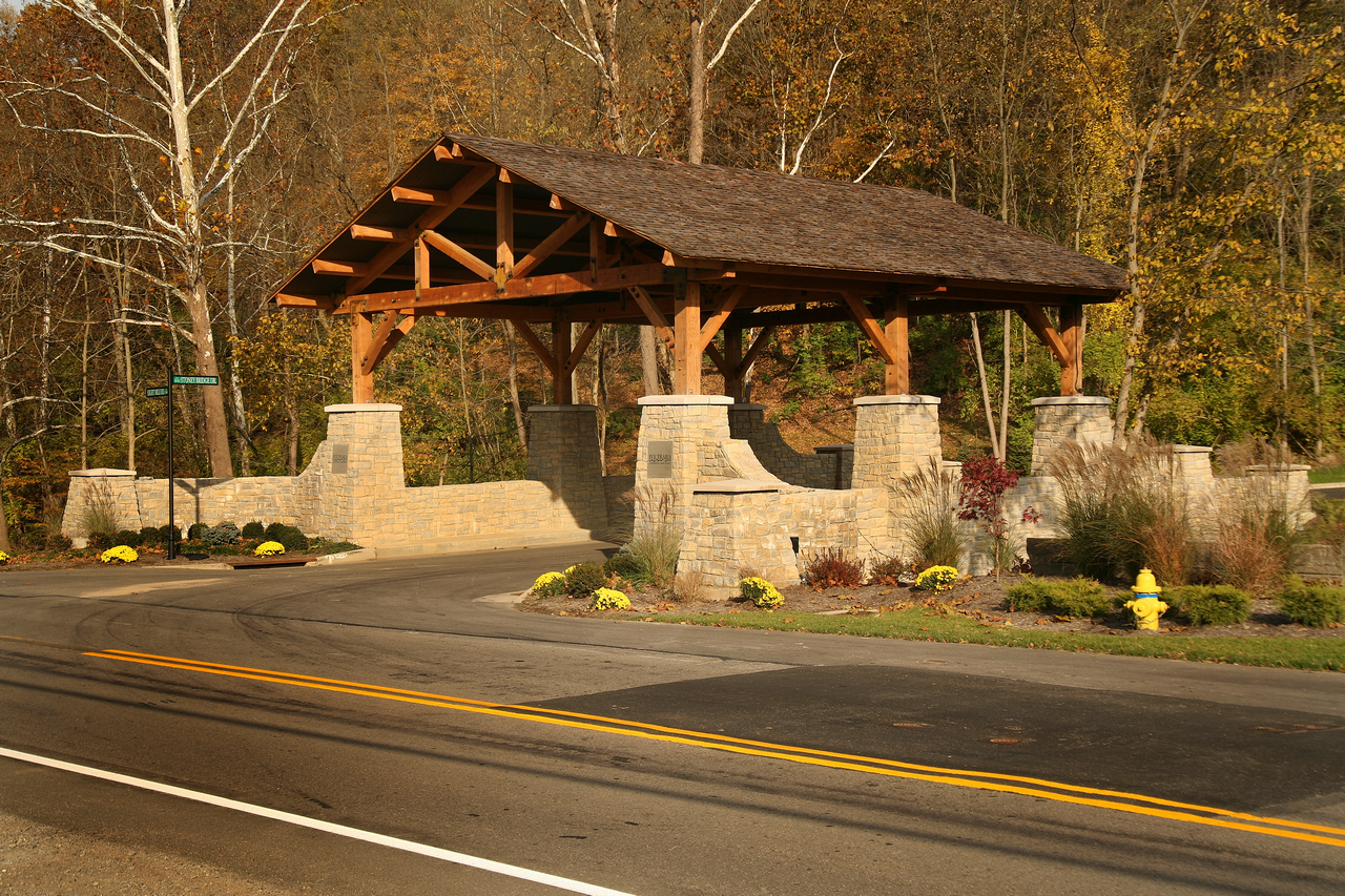Rustic stone and wood entrance gate on a road, surrounded by autumn trees.