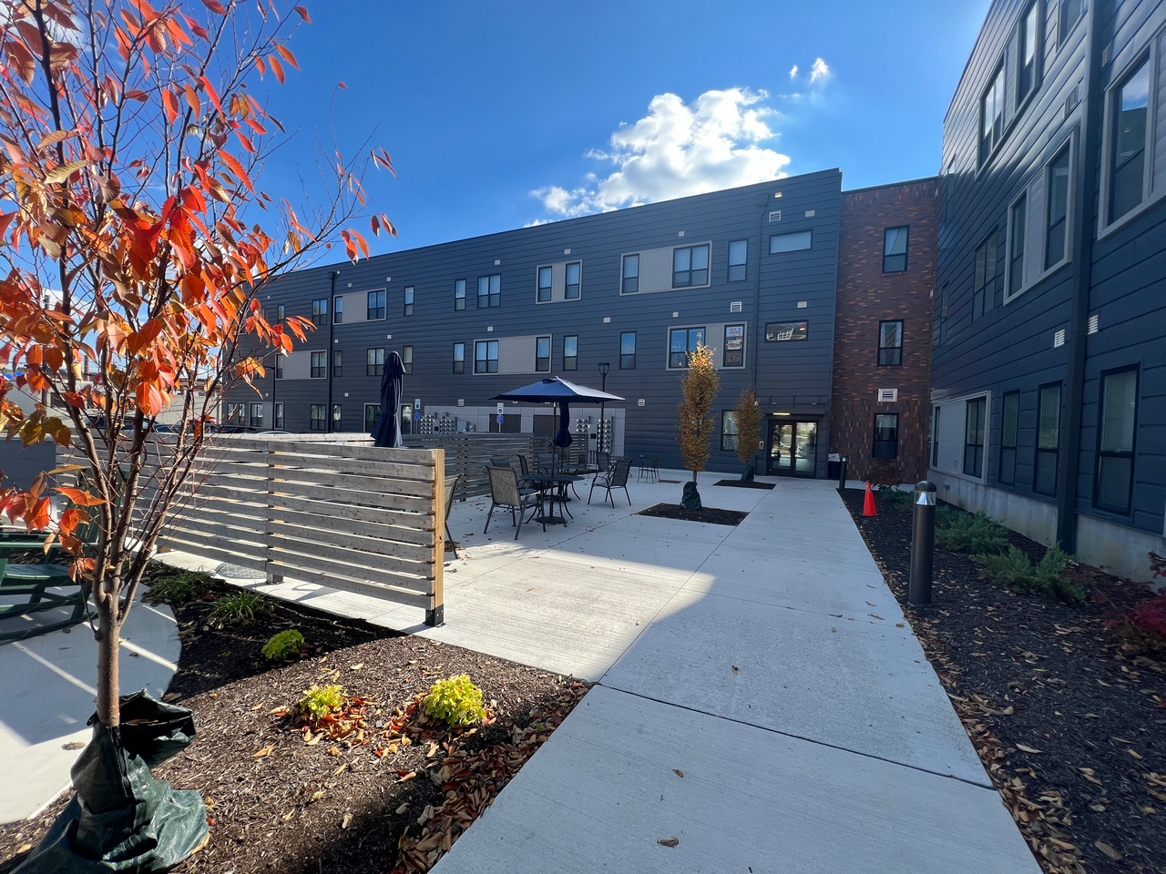 Courtyard with patio furniture, autumn tree, modern building, and clear blue sky.