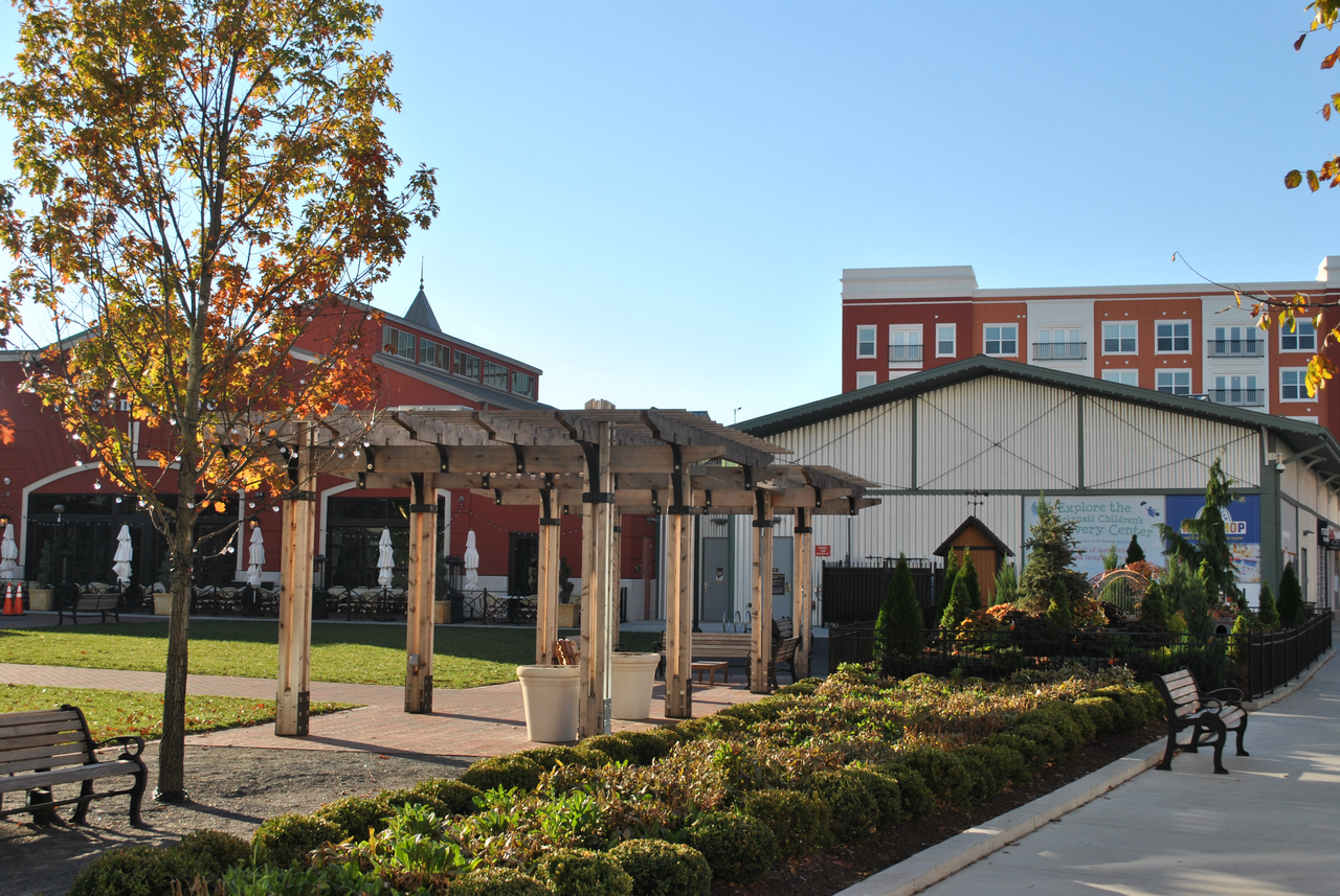 Courtyard with a pergola, trees, and surrounding buildings under a clear blue sky.